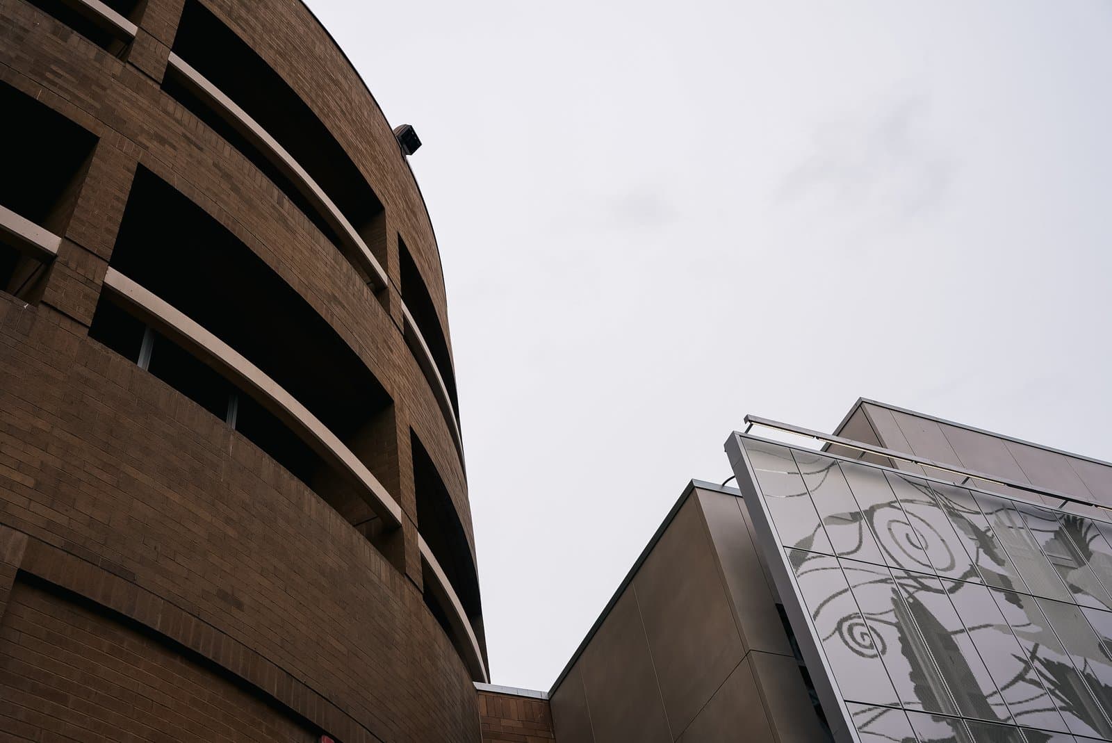 The curved brick facade of a parking structure stands beside a modern building with a decorative glass panel in Anchorage, Alaska.