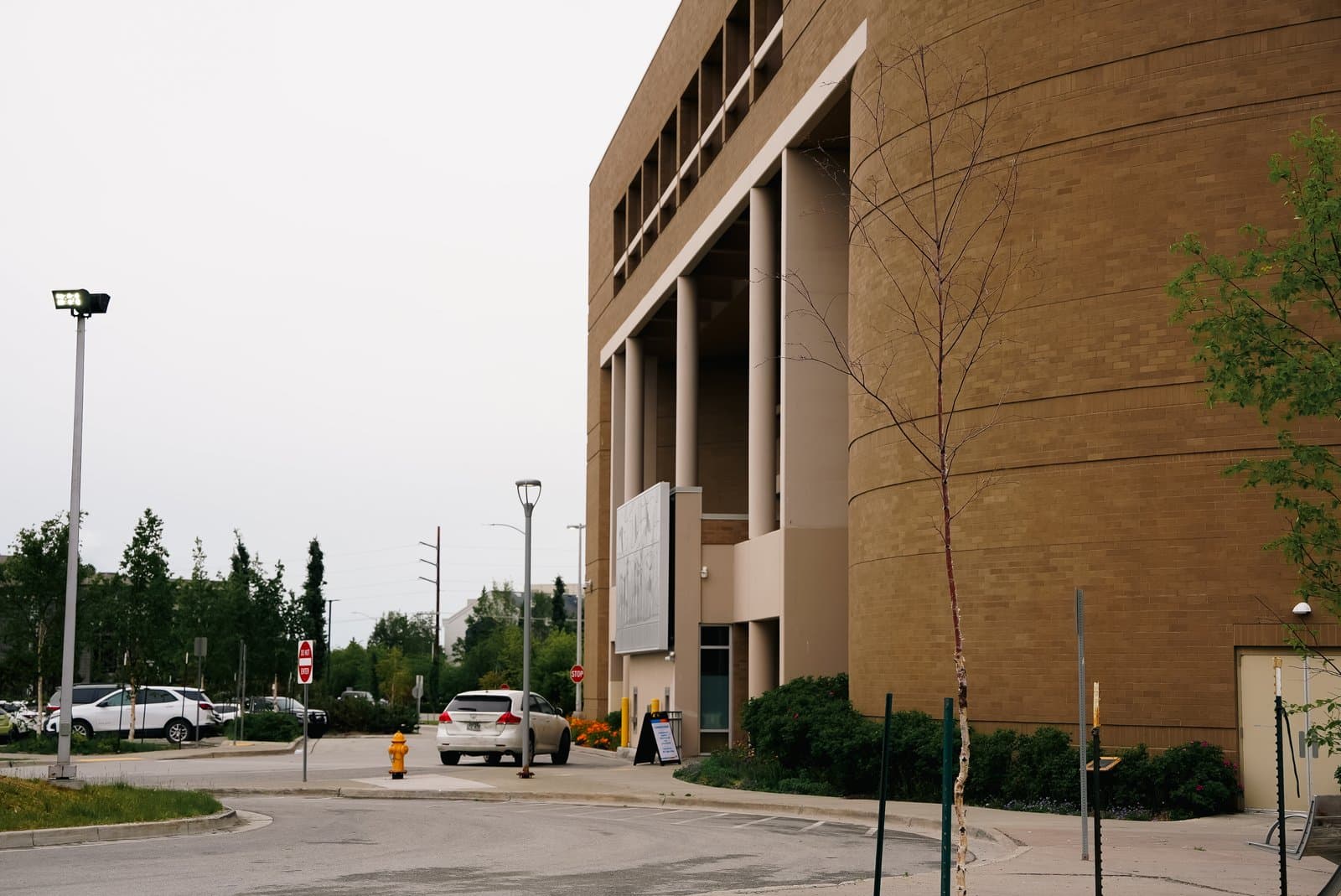 The exterior of a brick municipal building in Anchorage, Alaska, features a large entrance with columns and a parking lot on a summer day.