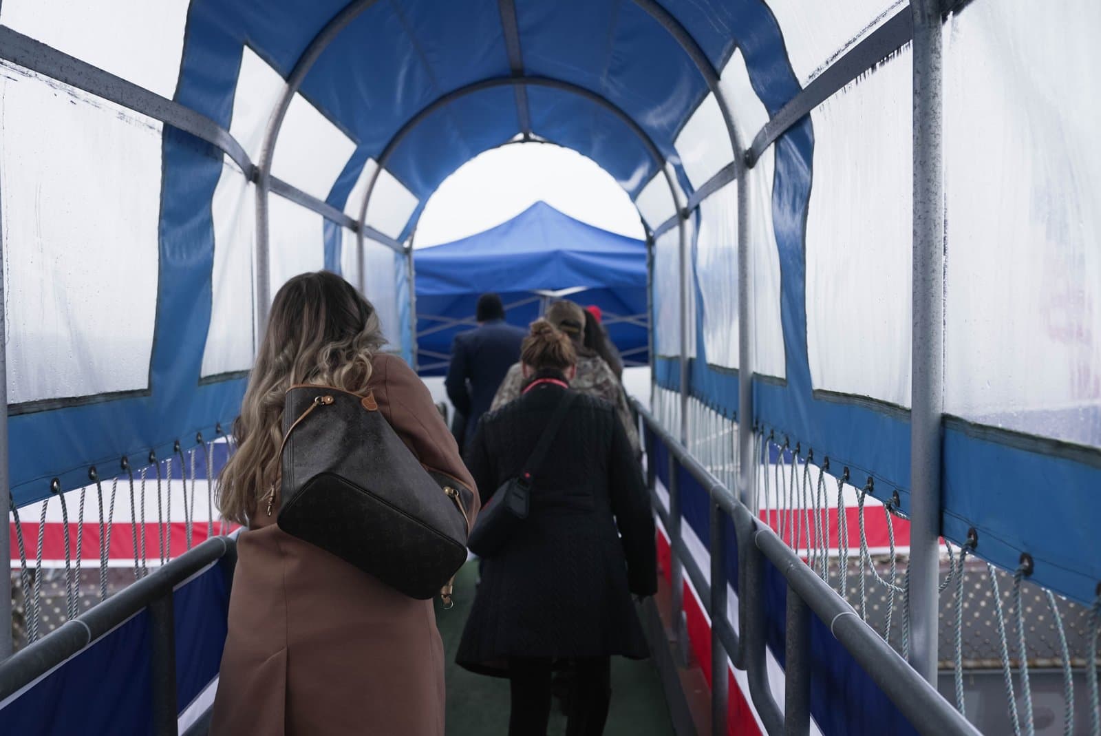 People walk through a covered, blue-and-white pedestrian walkway decorated with red, white, and blue bunting during an outdoor event.
