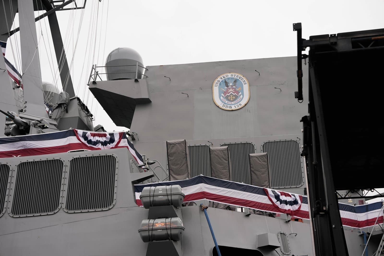 The superstructure of the USS Ted Stevens, a naval destroyer, displays its official crest and patriotic bunting during a formal ceremony.