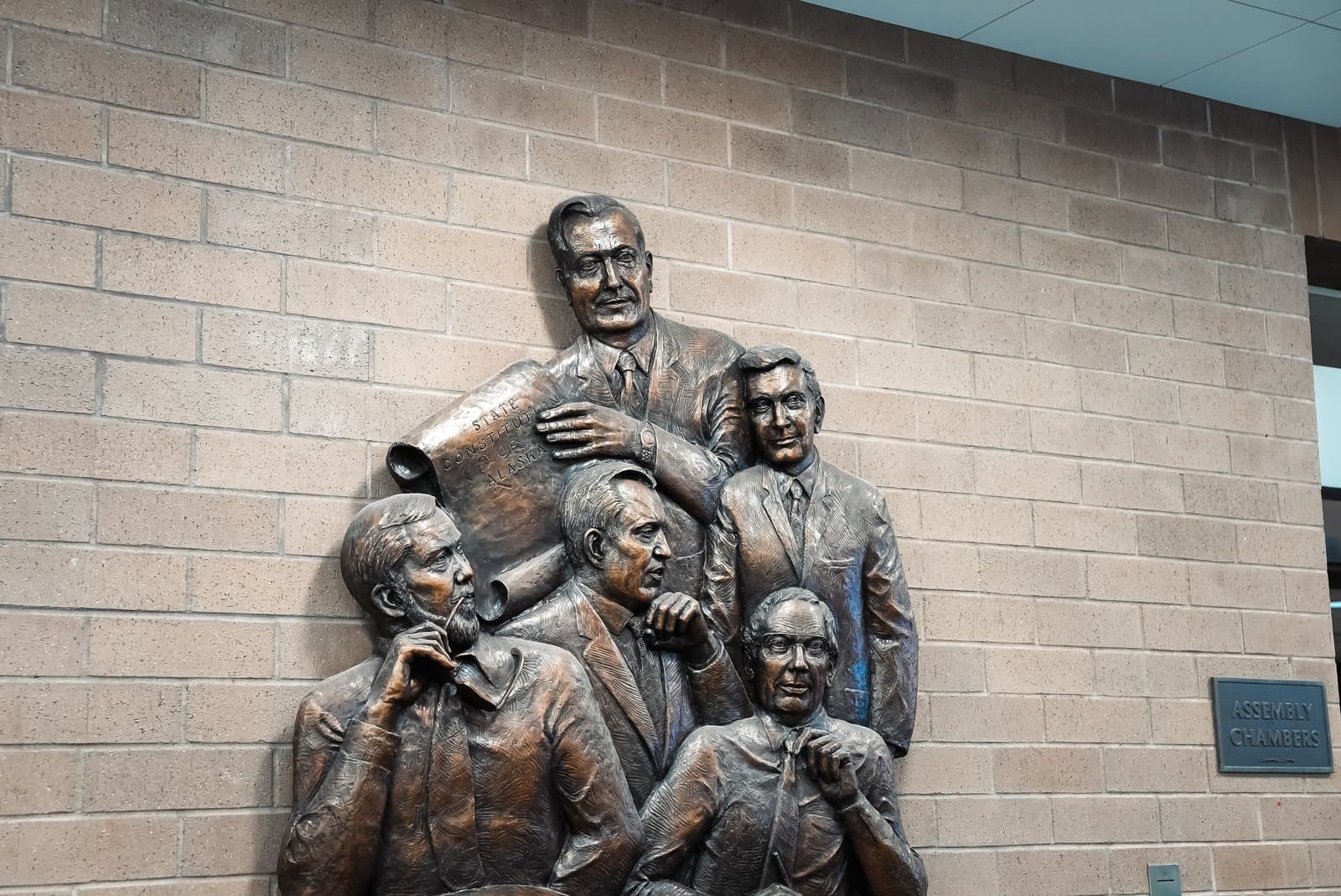 A bronze relief sculpture depicting five men holding a document titled State Constitution of Alaska mounted on a brick wall in Anchorage.