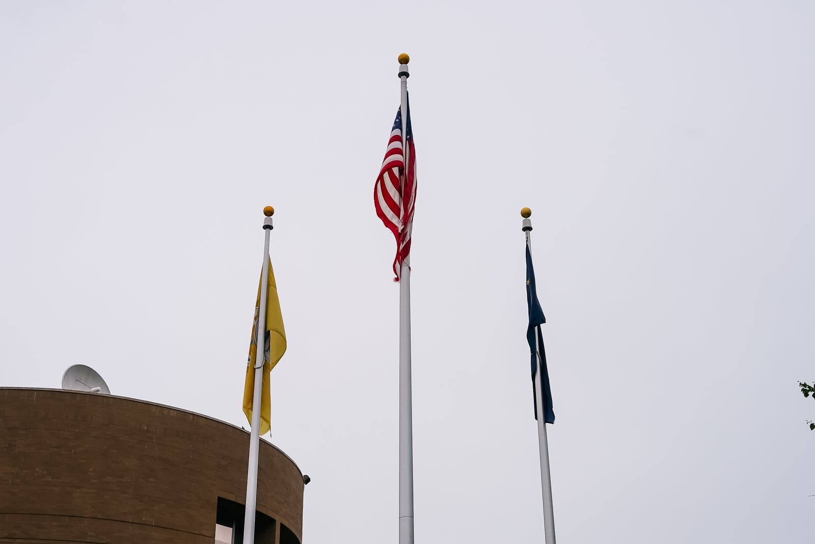 Three flags fly on poles outside a brick building during an Anchorage Assembly meeting on a cloudy June day in Anchorage, Alaska.