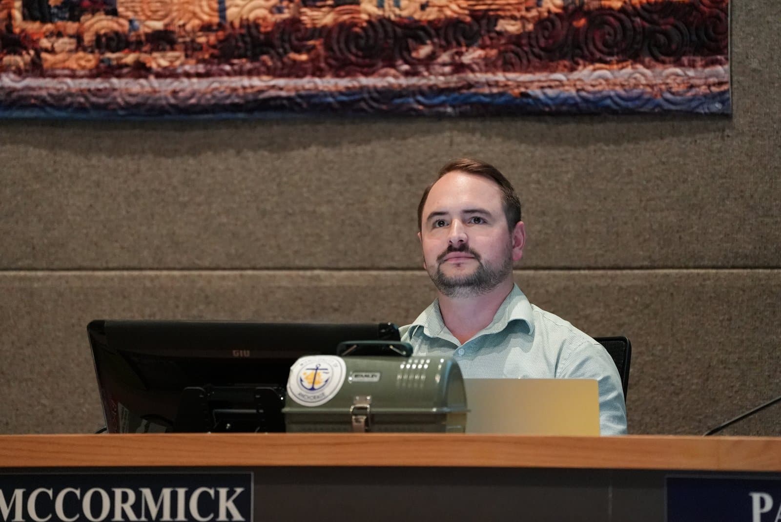 A man sits at a desk with a computer and a lunchbox during an Anchorage Assembly meeting in Anchorage, Alaska.