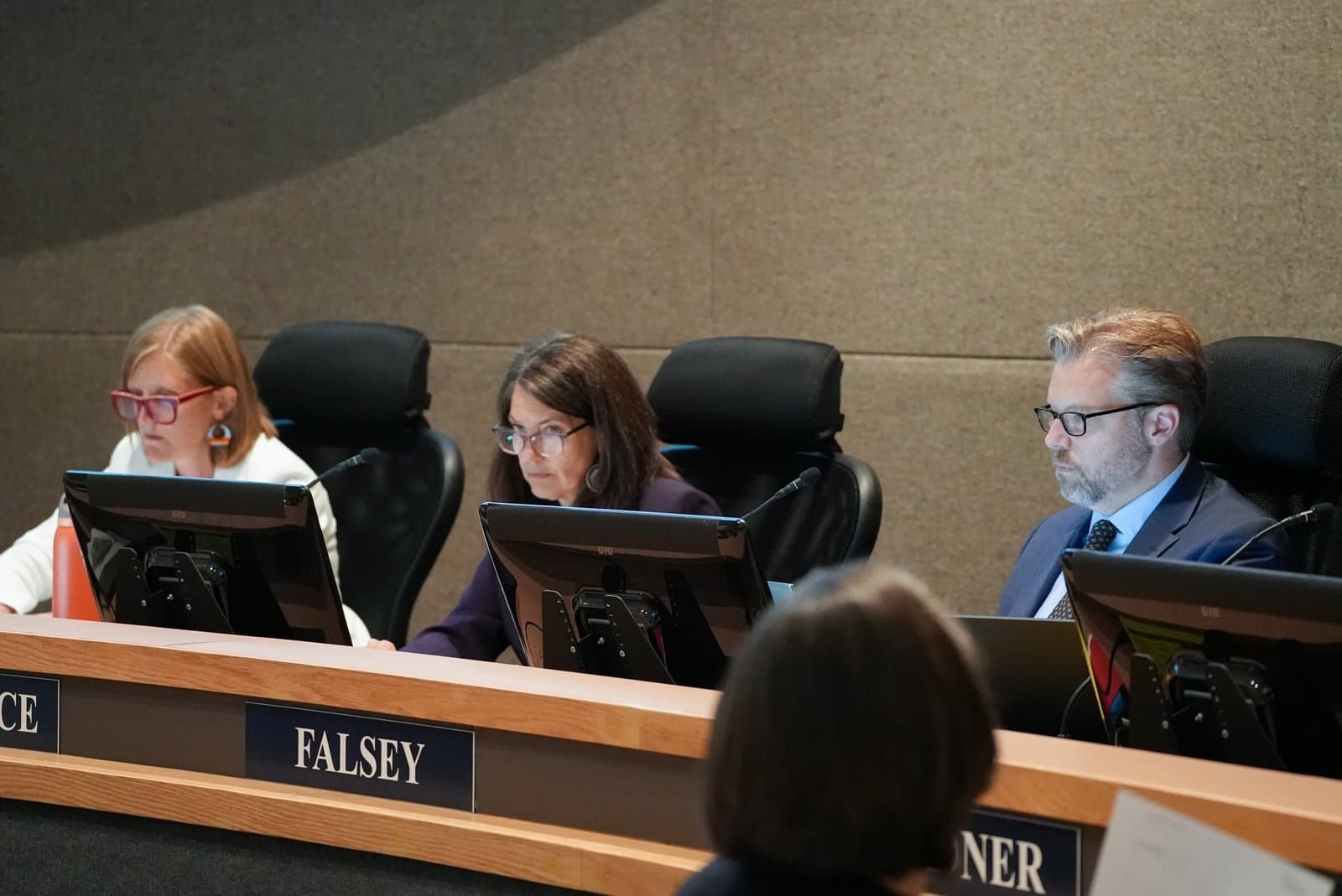 Three Anchorage Assembly members sit at a dais with computers and microphones during a public meeting held in Anchorage, Alaska.