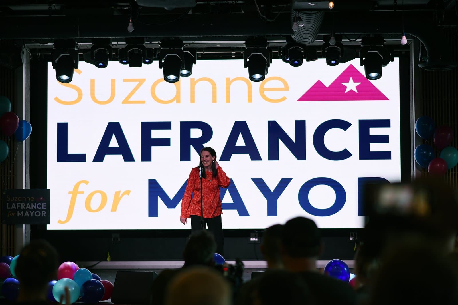 Suzanne LaFrance stands on a stage at her mayoral election night party in Anchorage, Alaska, in front of a large campaign sign.