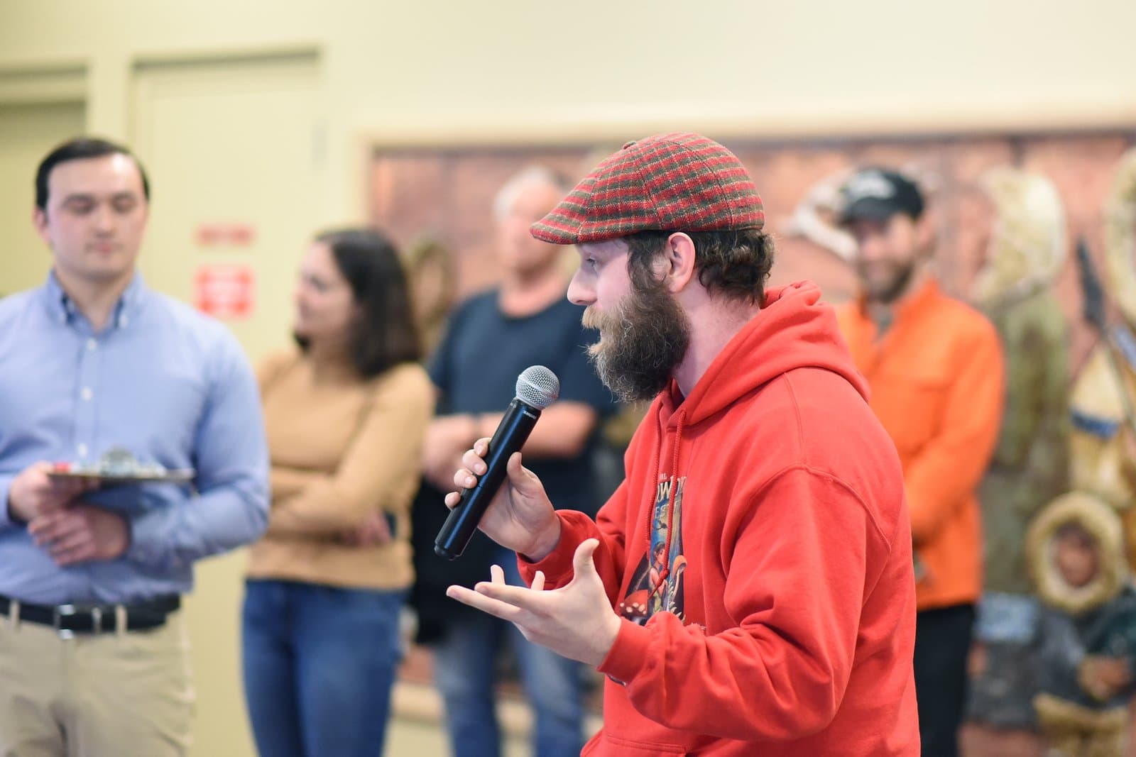 A man with a beard and a plaid cap speaks into a microphone during the 2024 Anchorage Legislative Town Hall meeting.