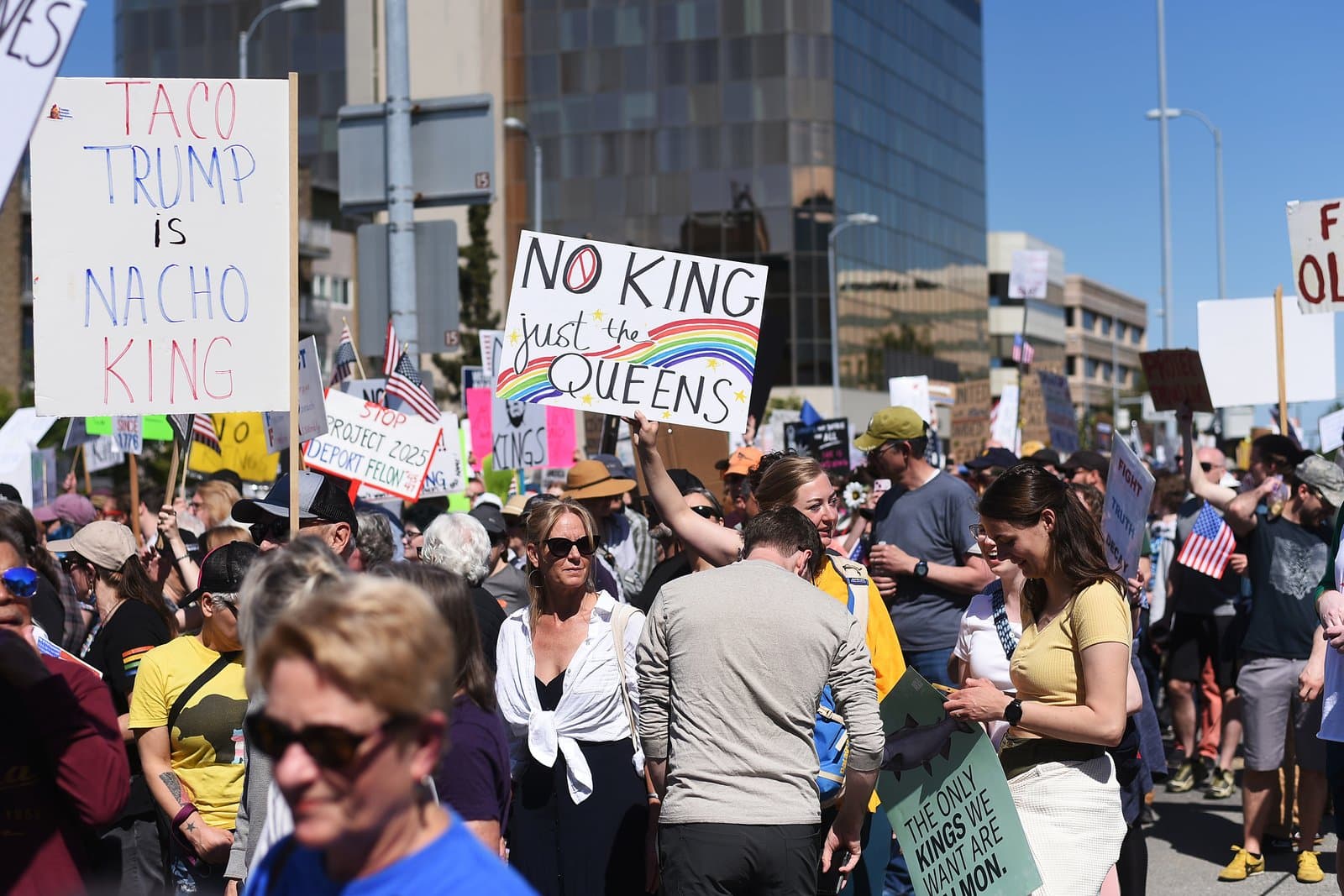 Protesters hold signs during a demonstration in Anchorage, Alaska, featuring messages about political figures and the phrase No Kings.