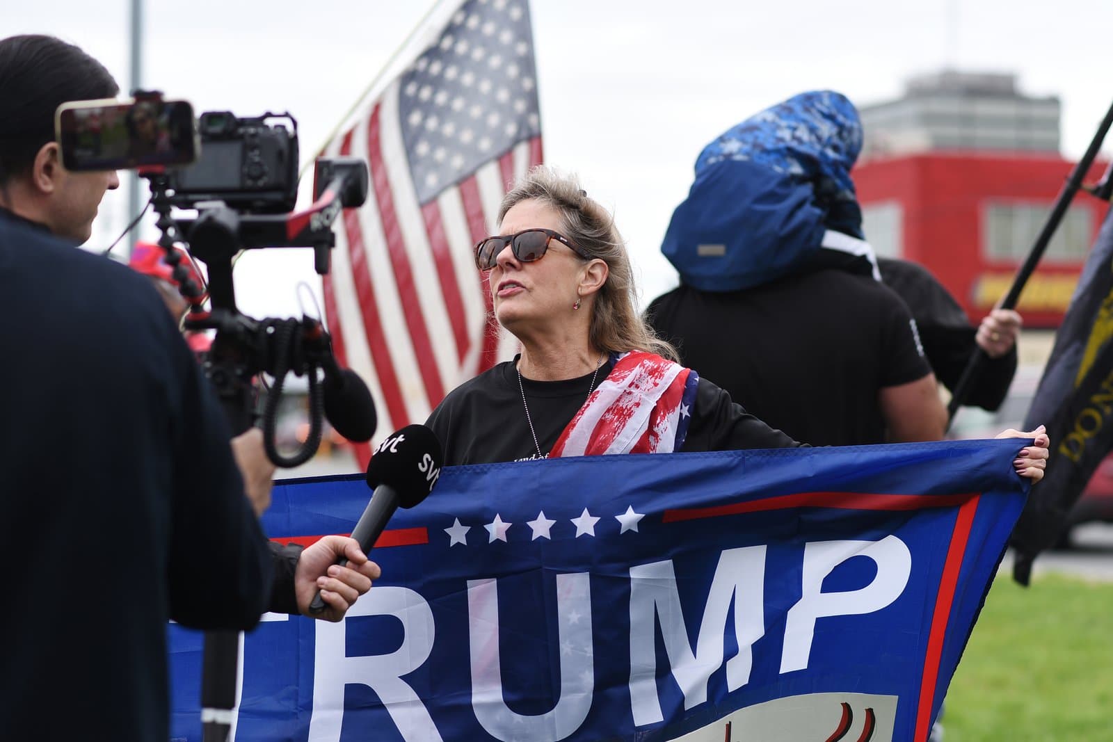 A woman holds a Trump flag while being interviewed by a reporter during a political rally in midtown Anchorage, Alaska.