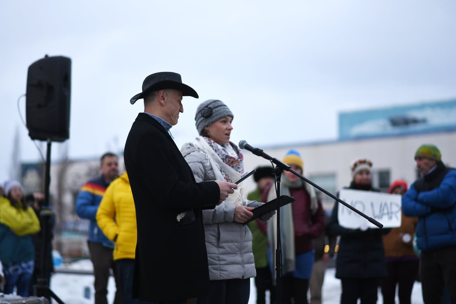 A man in a cowboy hat and a woman in a winter hat speak into a microphone at an Anchorage rally supporting Ukraine.