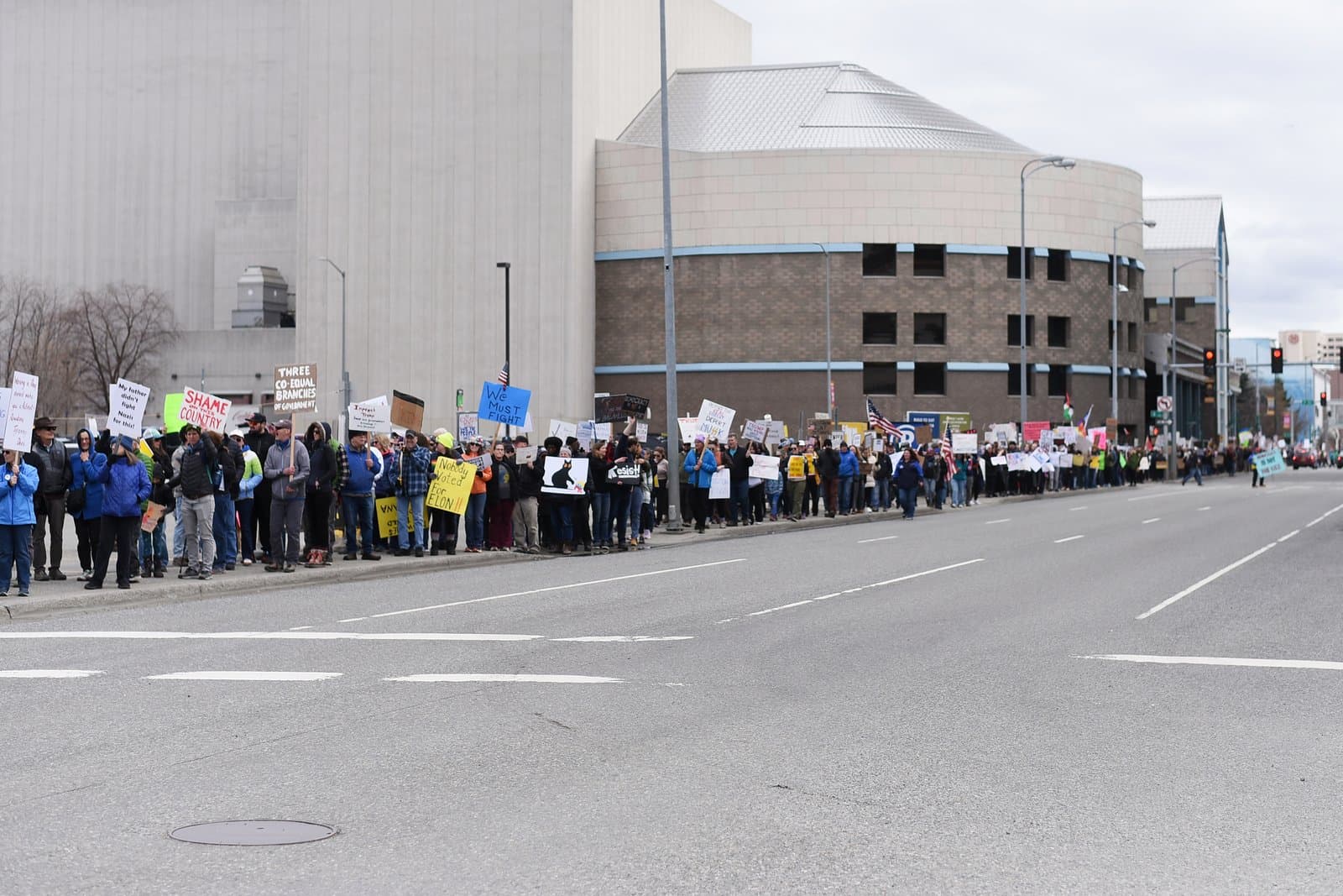A group of protesters holding signs stands along a city street in Anchorage during an organized demonstration on April 19, 2025.