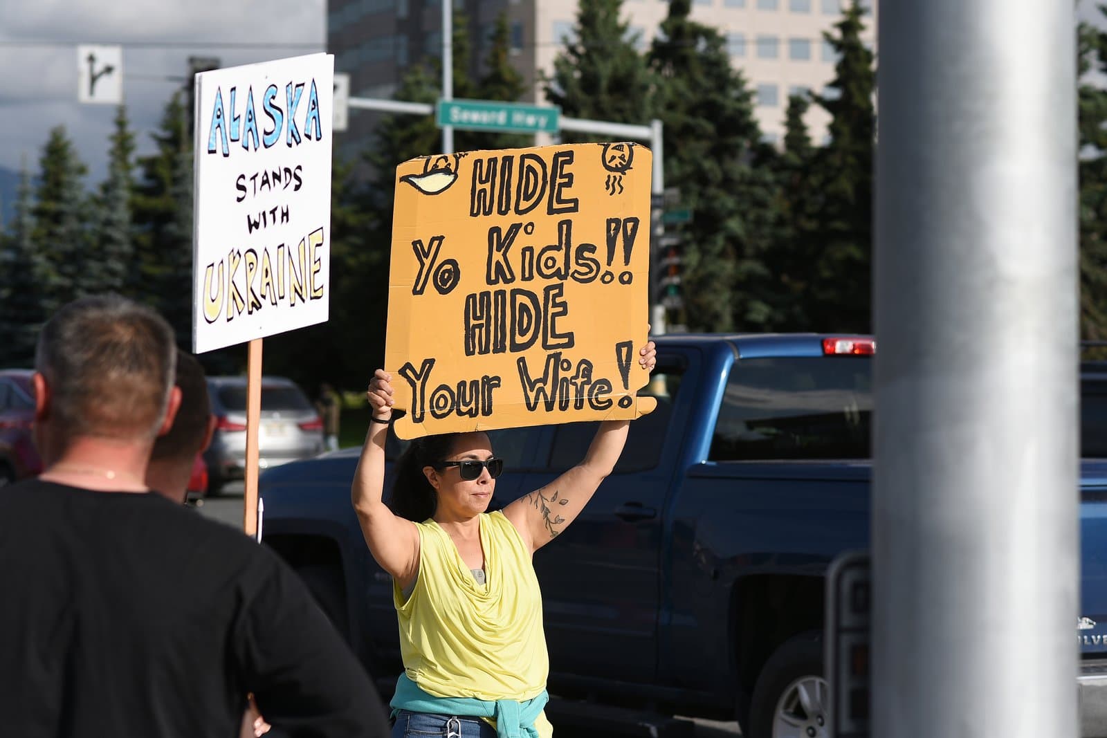 A woman holds a protest sign in midtown Anchorage while participating in a rally supporting Ukraine and opposing political figures.