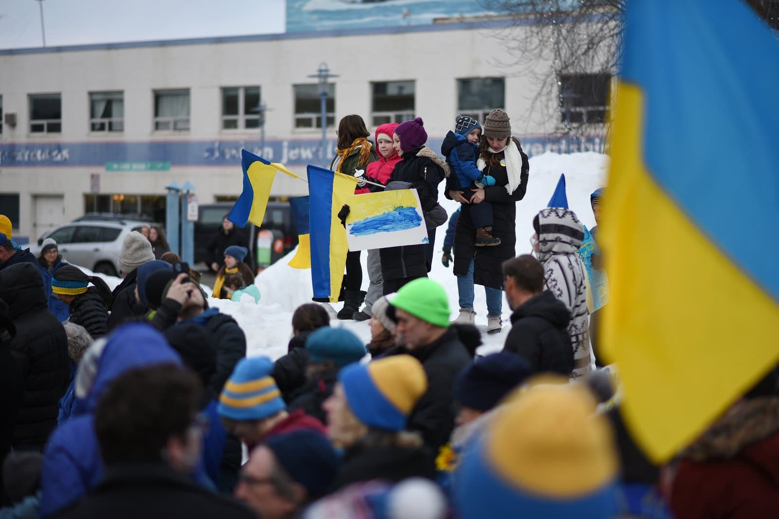 People gather in Anchorage, Alaska, holding Ukrainian flags and signs during a community rally in support of Ukraine amidst snowy conditions.