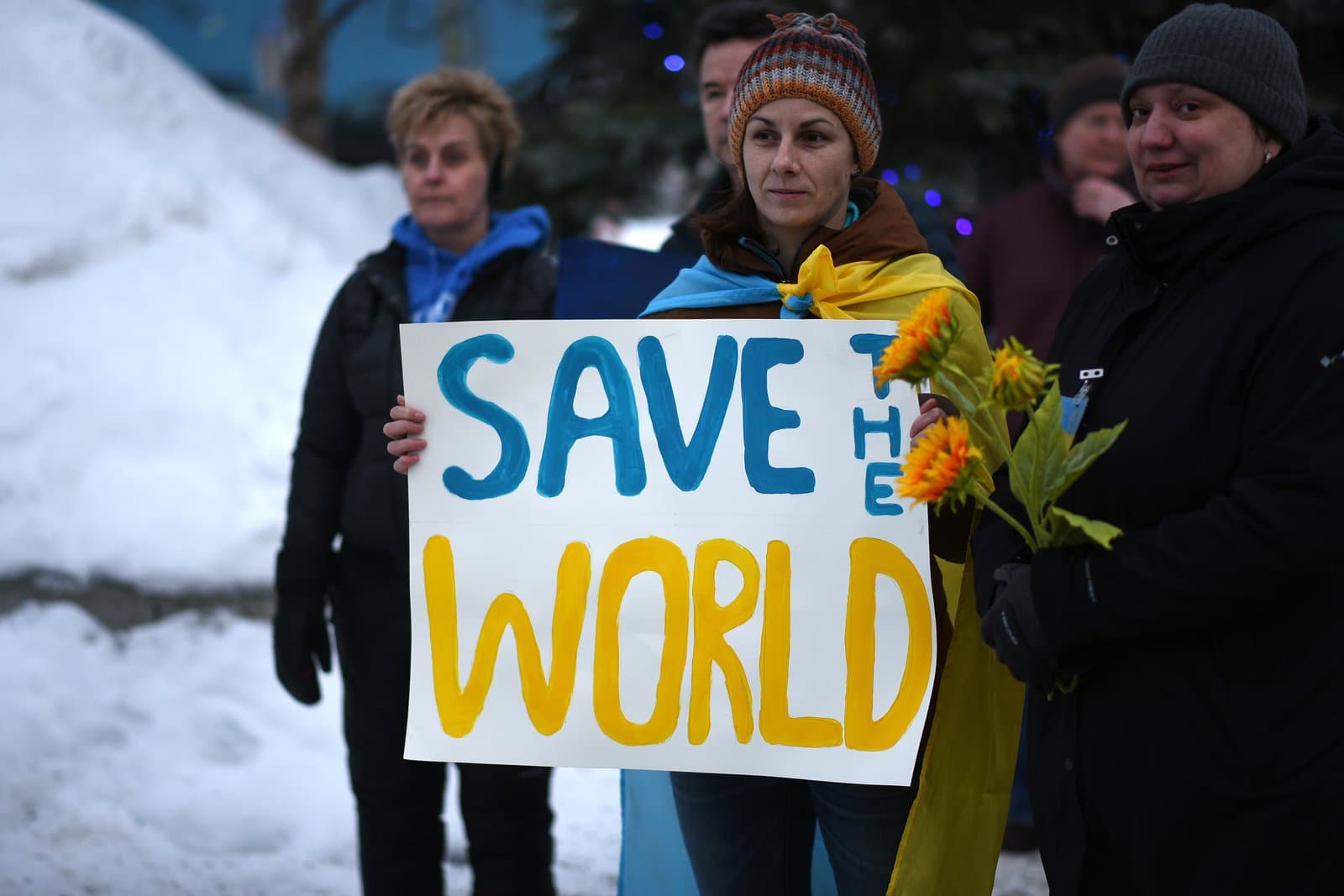 A woman holds a Save the World sign while standing with others during a rally in support of Ukraine in Anchorage, Alaska.