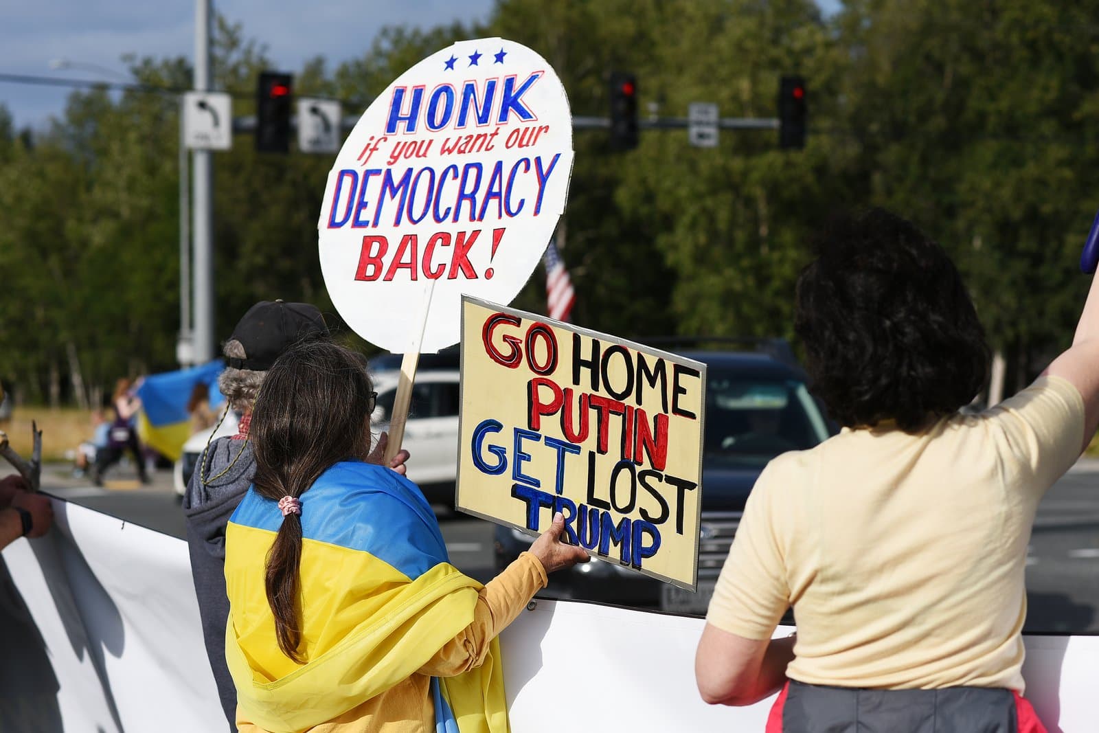Protesters hold signs advocating for democracy and criticizing political figures during a rally in midtown Anchorage, Alaska, in August 2025.