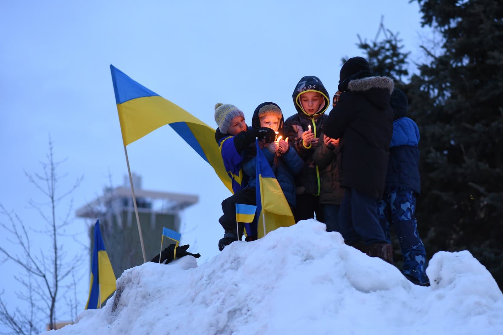 Children stand on a snowbank in Anchorage holding Ukrainian flags and lighting candles during a community vigil for Ukraine.