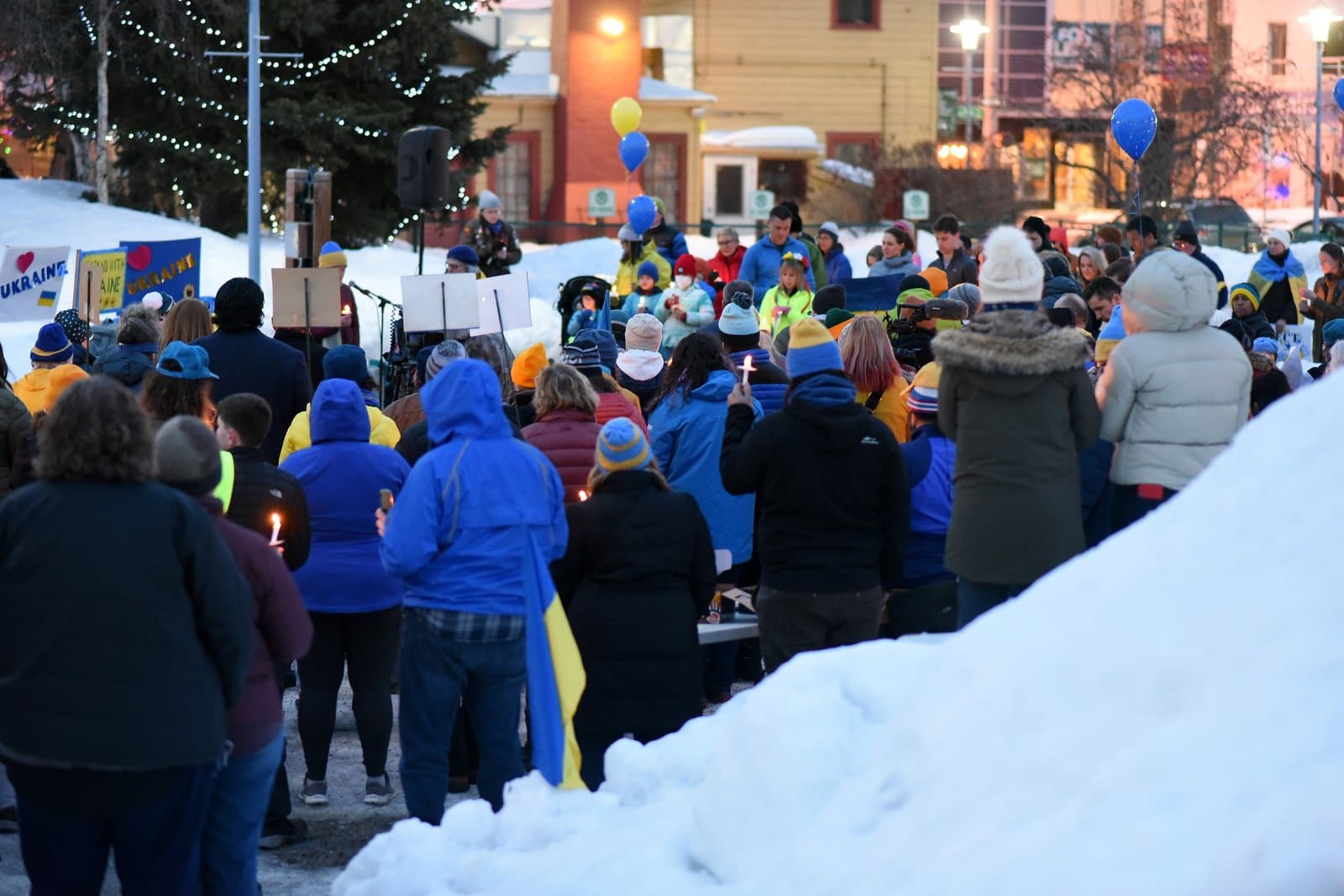 A crowd of people gathers in a snowy Anchorage park for a candlelight vigil in support of Ukraine.
