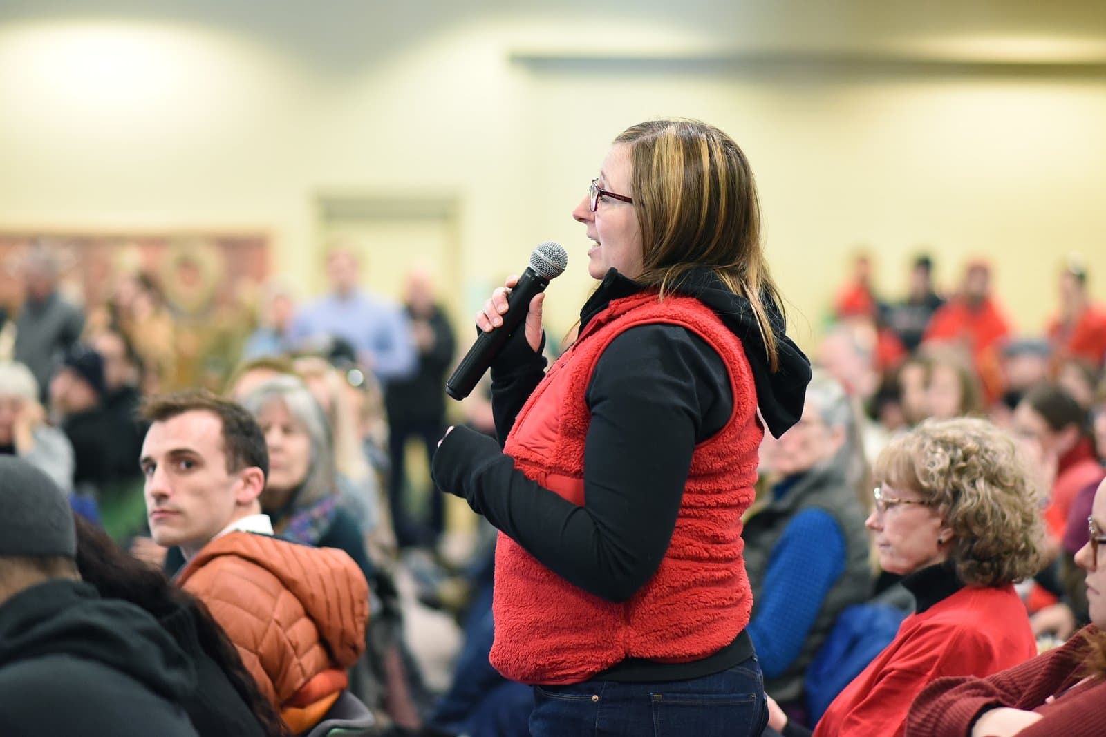 A woman speaks into a microphone during the 2024 Anchorage Legislative Town Hall, addressing an audience in a community meeting space.