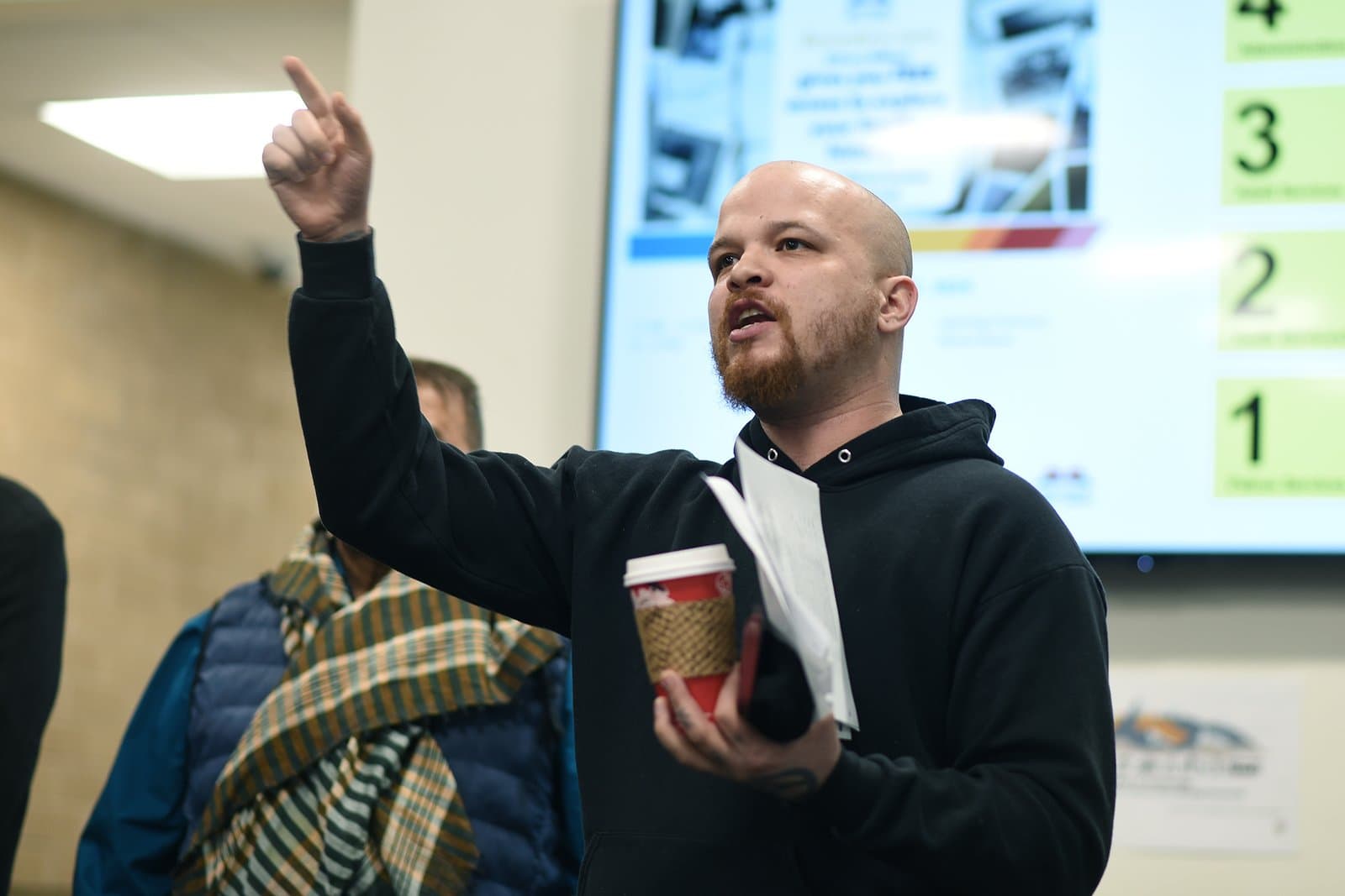 Michael Patterson speaks to supporters while holding papers and a coffee cup outside the Assembly chambers in Anchorage, Alaska.