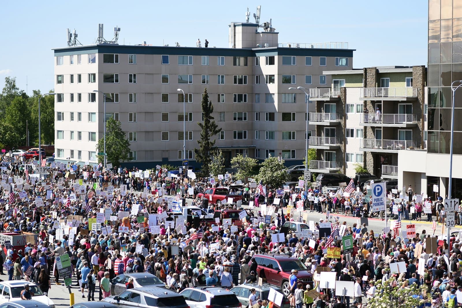 A large crowd of protesters holding signs gathers in an Anchorage parking lot during the No Kings demonstration on June 14, 2025.