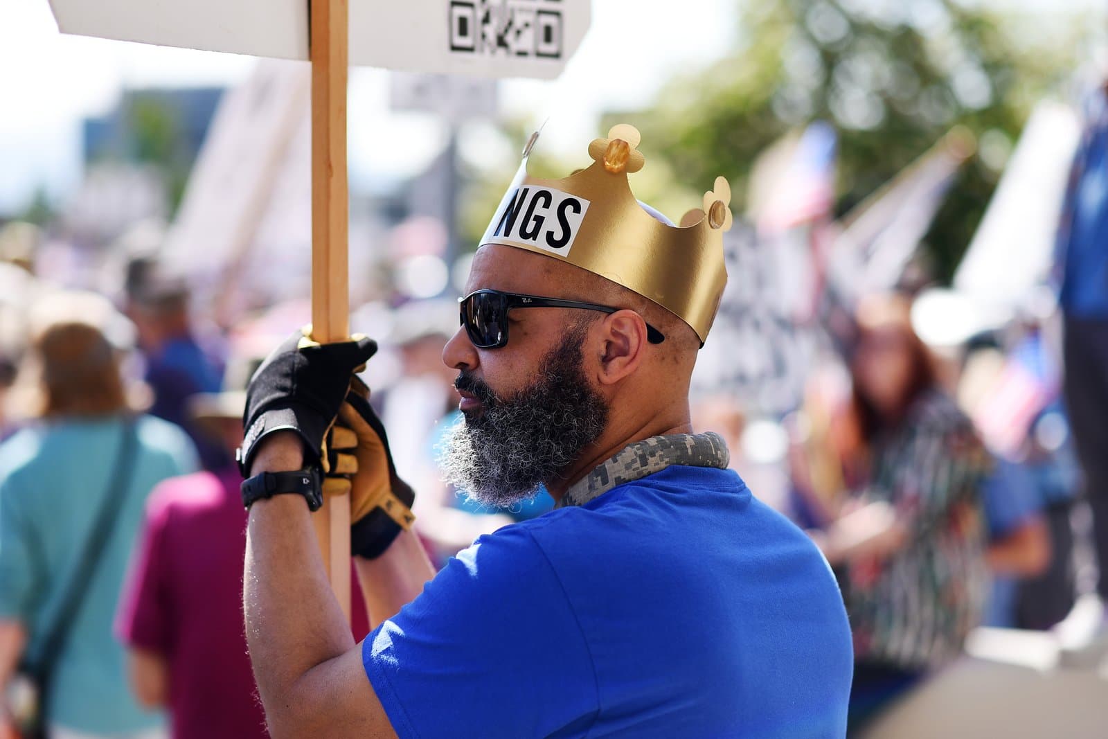 A protester wearing a gold paper crown labeled "NGS" holds a sign during a "No Kings" demonstration in Anchorage, Alaska.