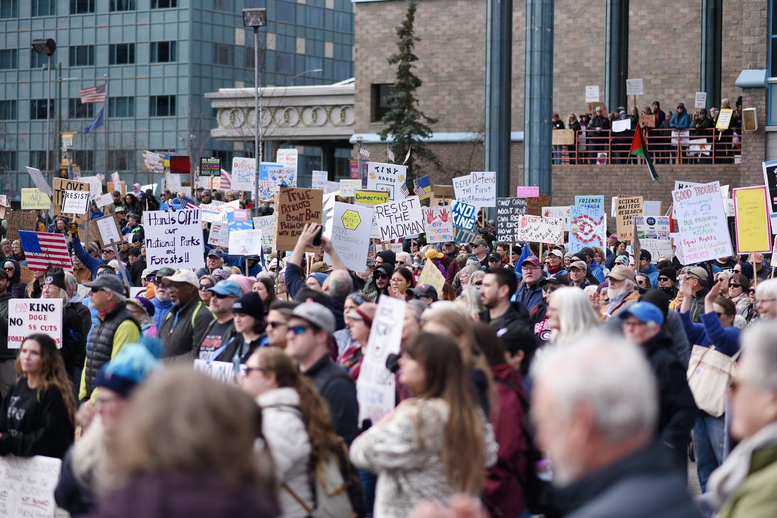 A large crowd of protesters holds various signs during a public demonstration in downtown Anchorage on a spring afternoon in April.