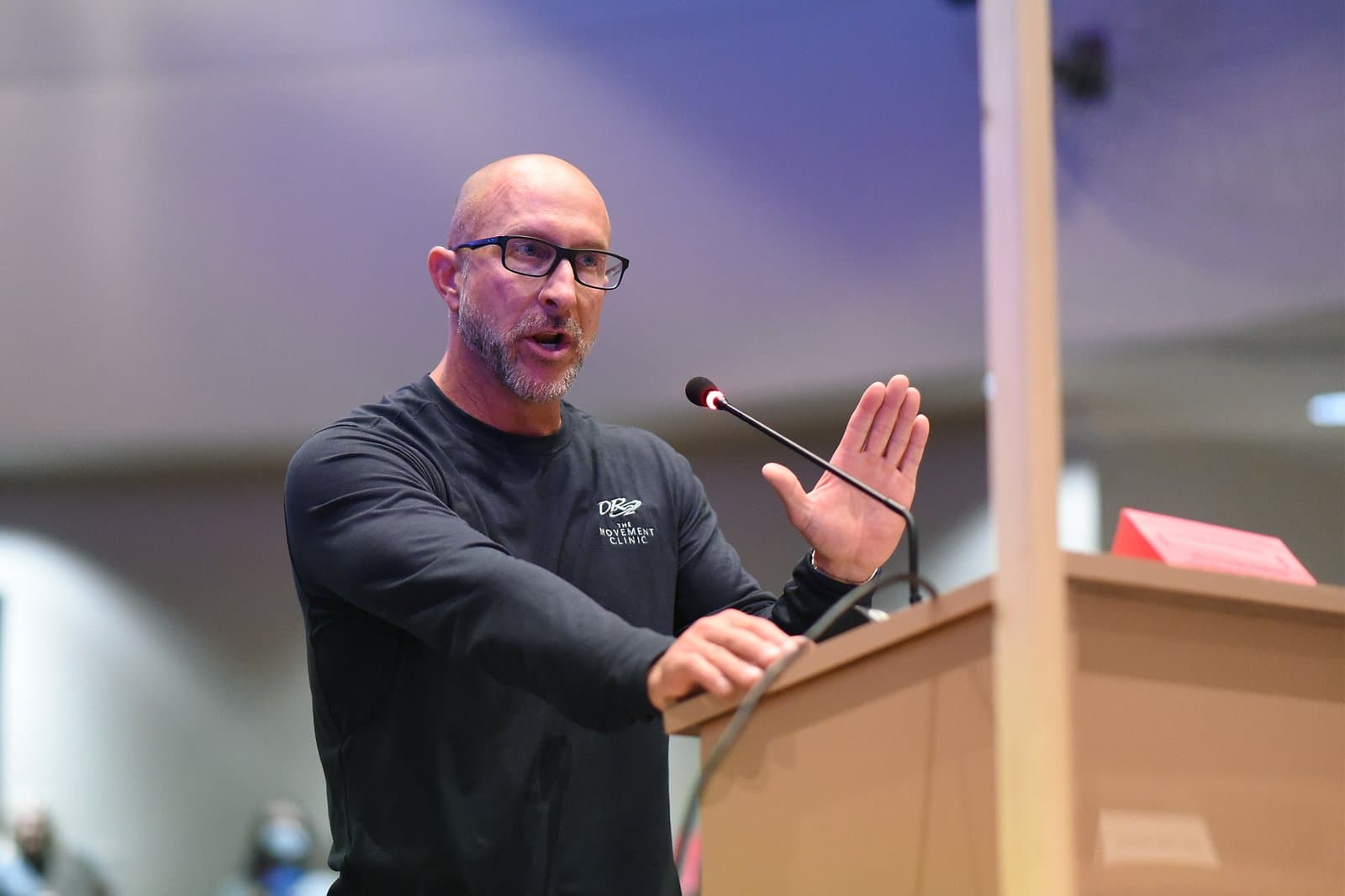 A man wearing a Movement Clinic shirt speaks into a microphone at an Anchorage Assembly meeting in October 2021.