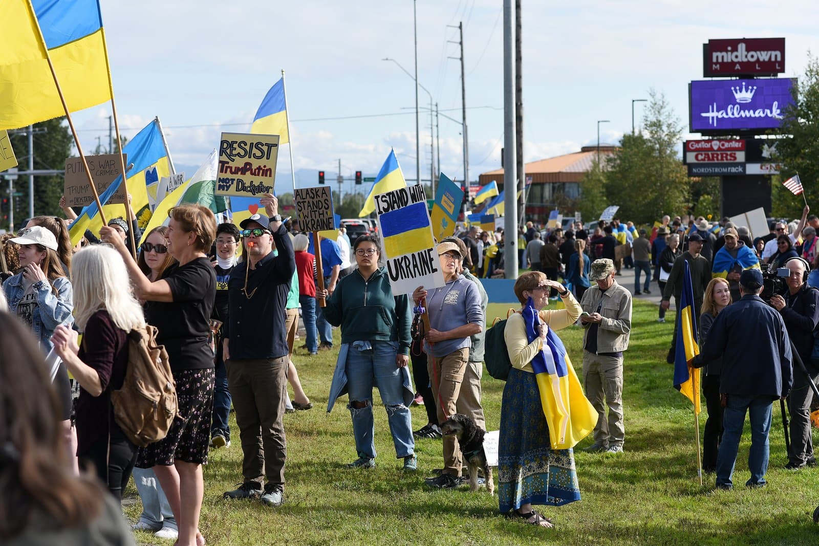 Protesters gather in a grassy area in midtown Anchorage, holding signs and Ukrainian flags during a rally on August 14, 2025.