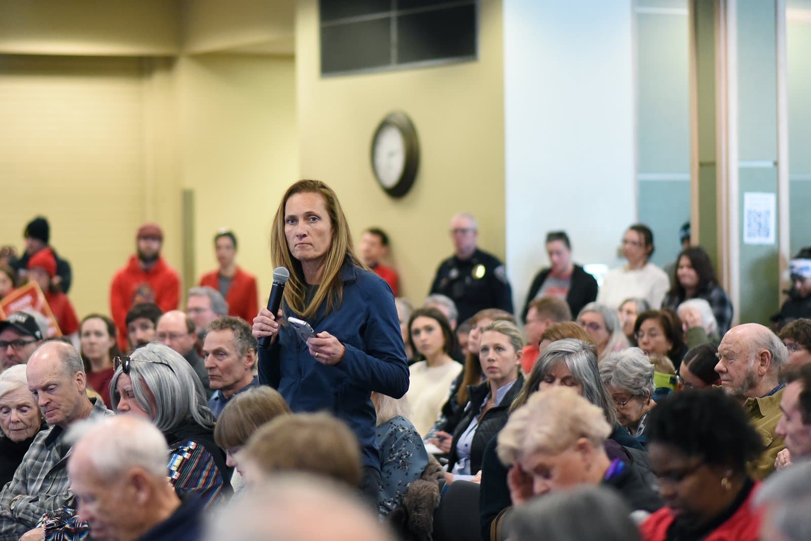 A woman holds a microphone while addressing an audience during the 2024 Anchorage Legislative Town Hall held in an indoor community space.