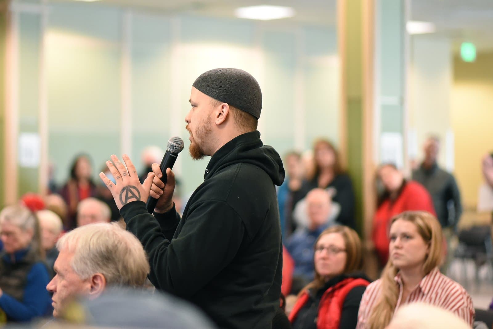 A man with a beard and a skullcap speaks into a microphone during the 2024 Anchorage Legislative Town Hall meeting.