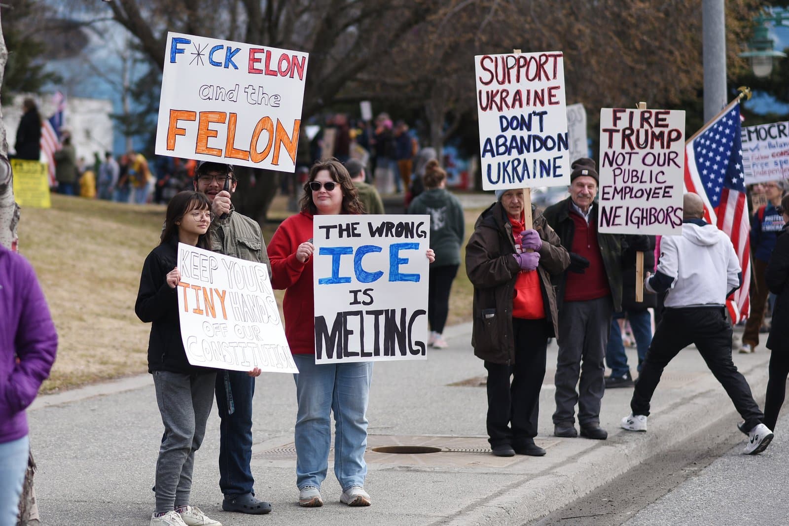 Protesters hold signs with political messages during a demonstration in Anchorage, Alaska, on a spring day in April 2025.