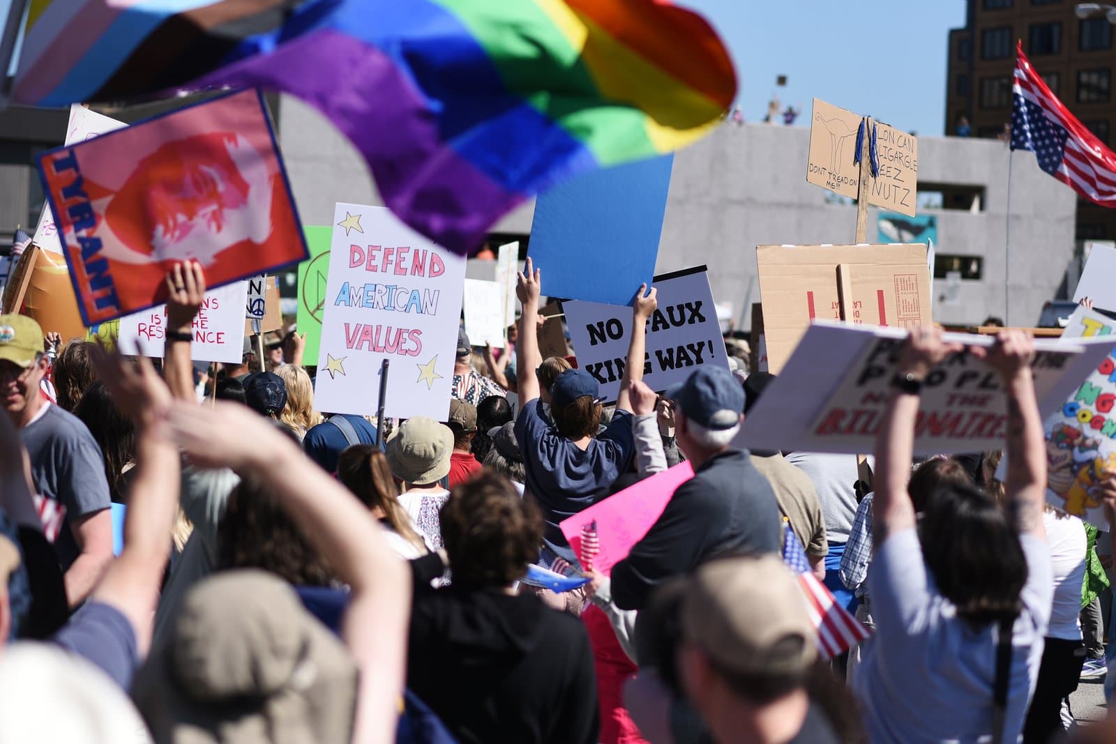Protesters hold signs and flags during a public demonstration in Anchorage, Alaska, on a sunny day in June 2025.