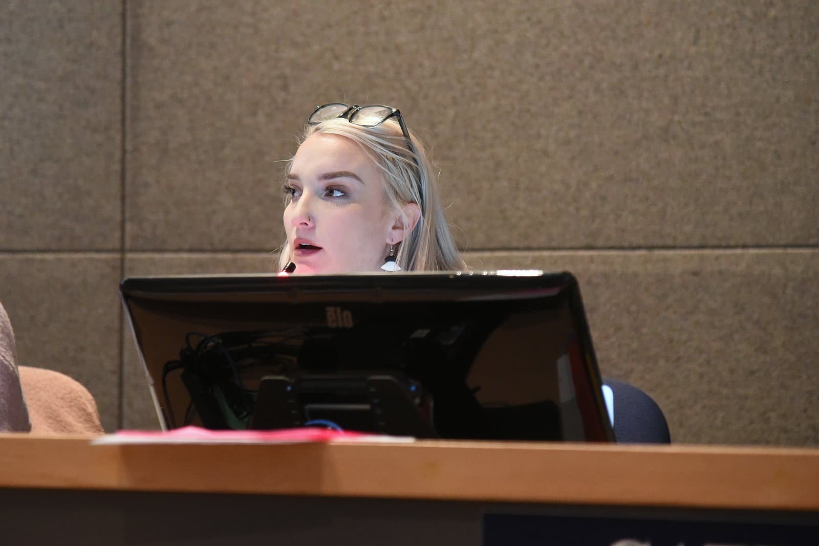 Alexis Johnson speaks at a public meeting in Anchorage, Alaska, while seated behind a desk with a computer monitor.