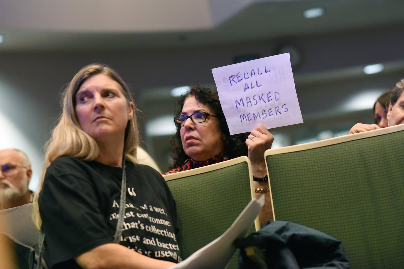 A woman holds a sign reading Recall All Masked Members during an Anchorage Assembly meeting held in October 2021.