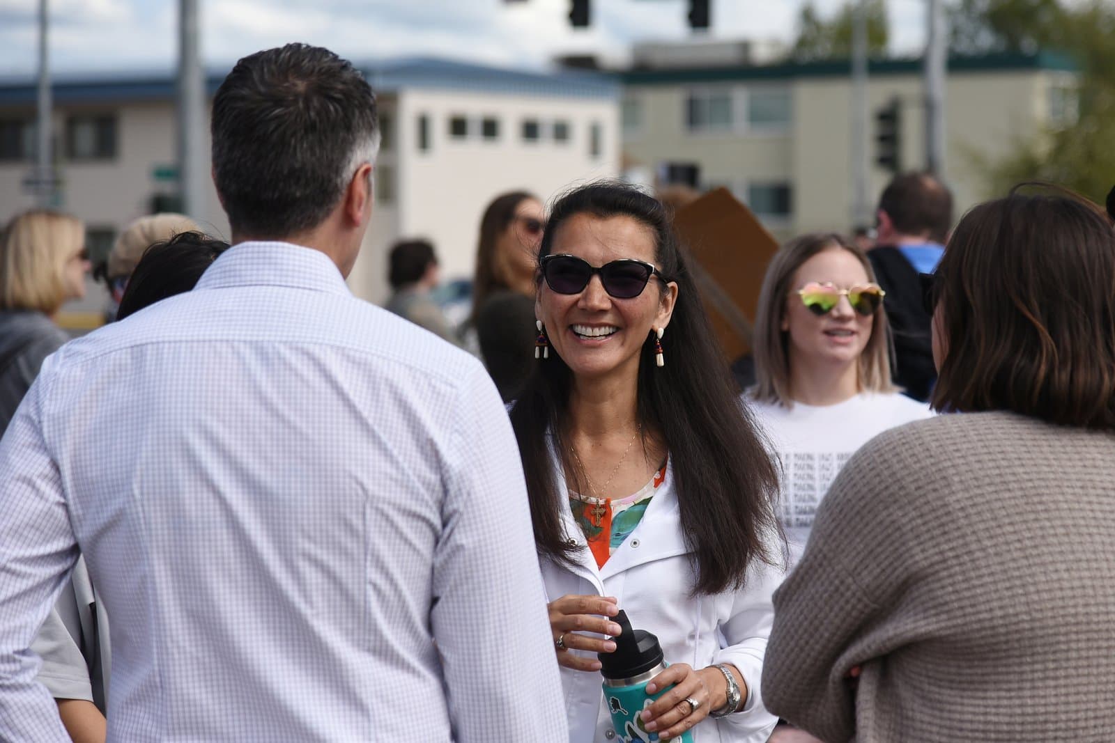 A smiling woman wearing sunglasses and a white jacket participates in a Planned Parenthood rally in downtown Anchorage, Alaska, on July 9, 2022.
