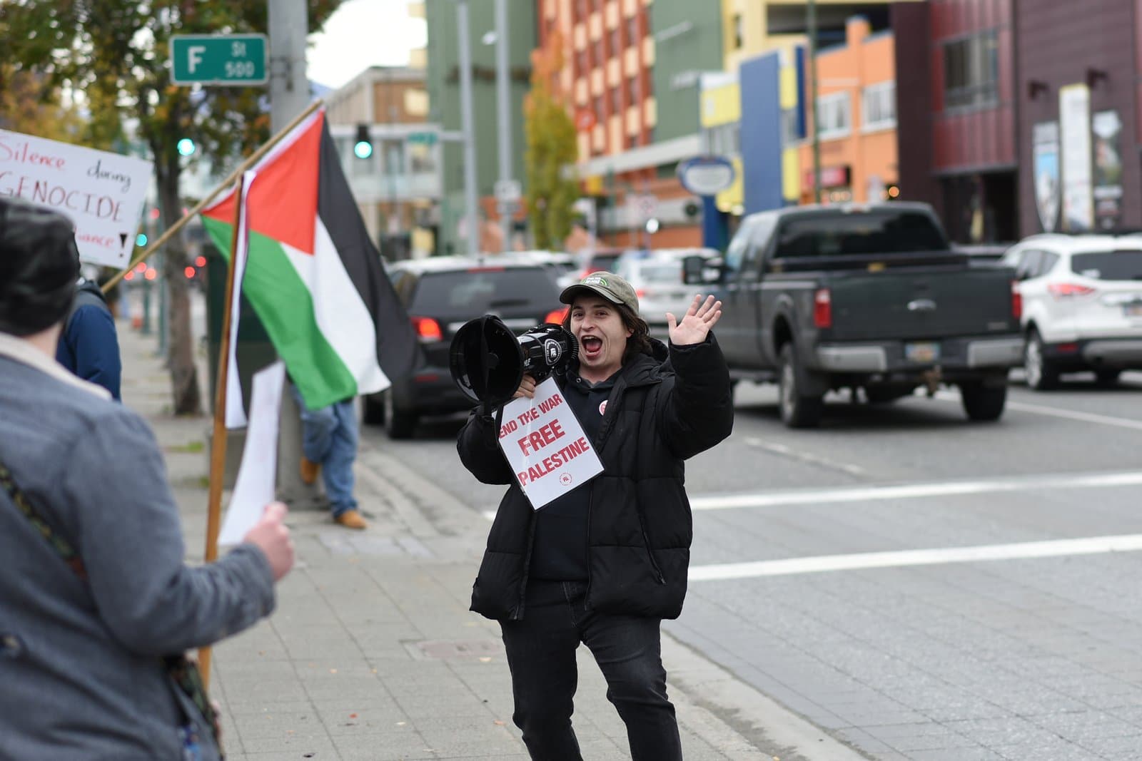A protester holding a megaphone and a sign reading End the War Free Palestine participates in a demonstration in downtown Anchorage, Alaska.