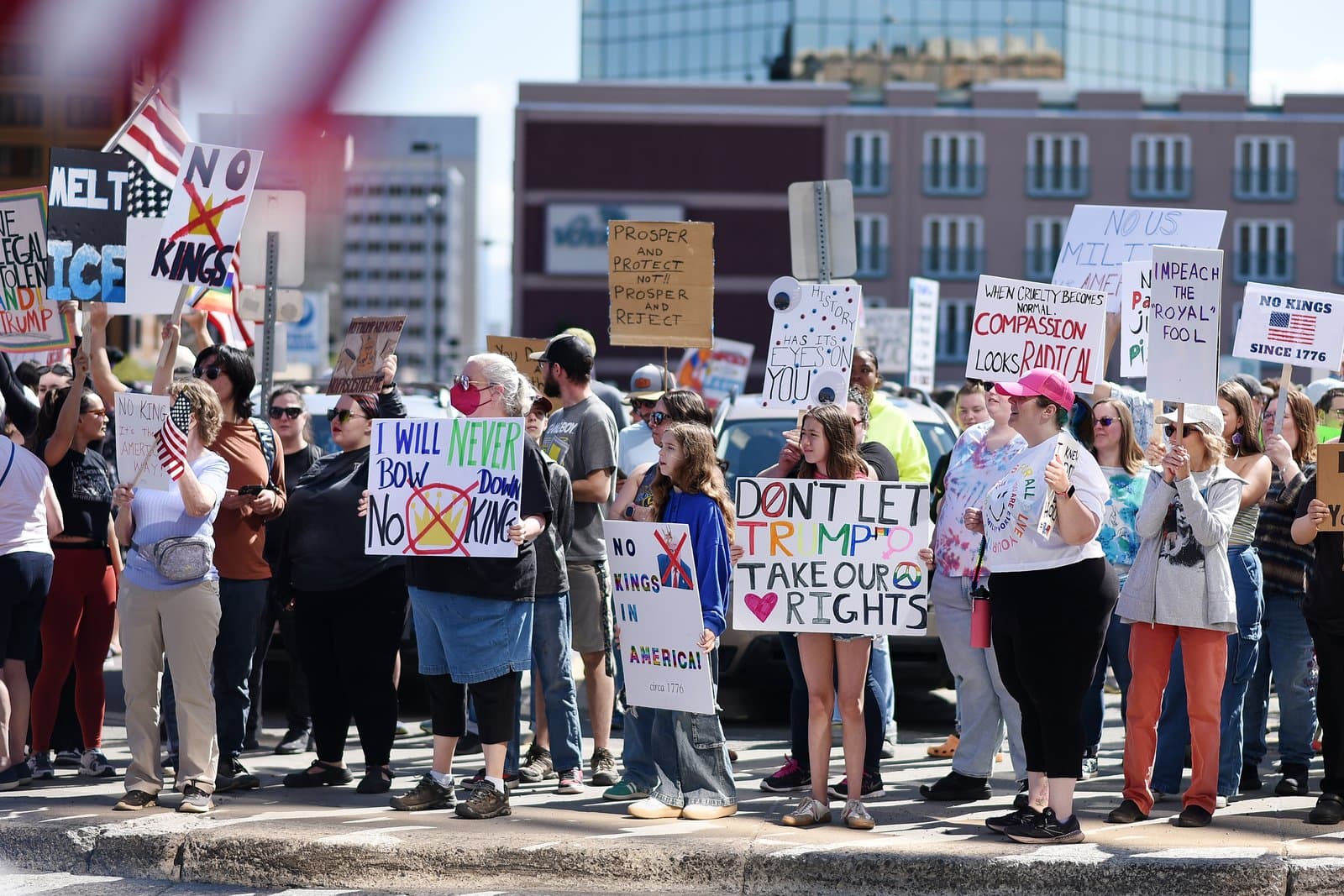 Protesters hold signs with political slogans during a No Kings rally on a sunny day in downtown Anchorage, Alaska.