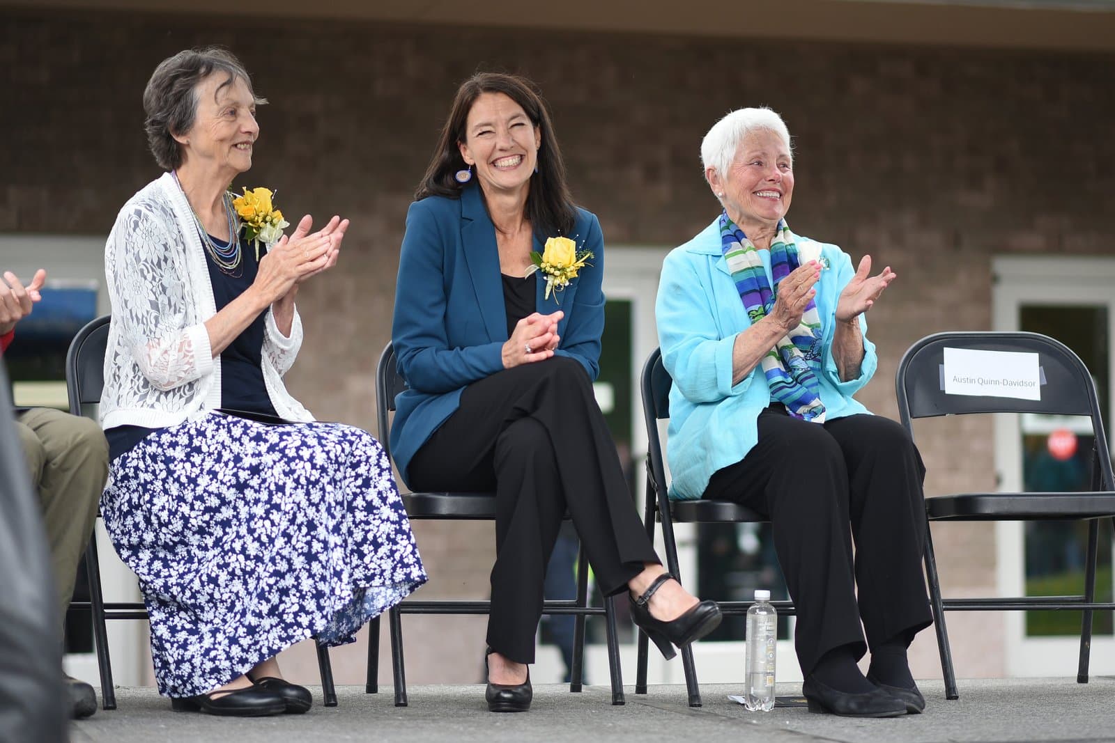 Anchorage Mayor Suzanne LaFrance sits in a chair and applauds alongside two other women during an outdoor community event in Anchorage, Alaska.