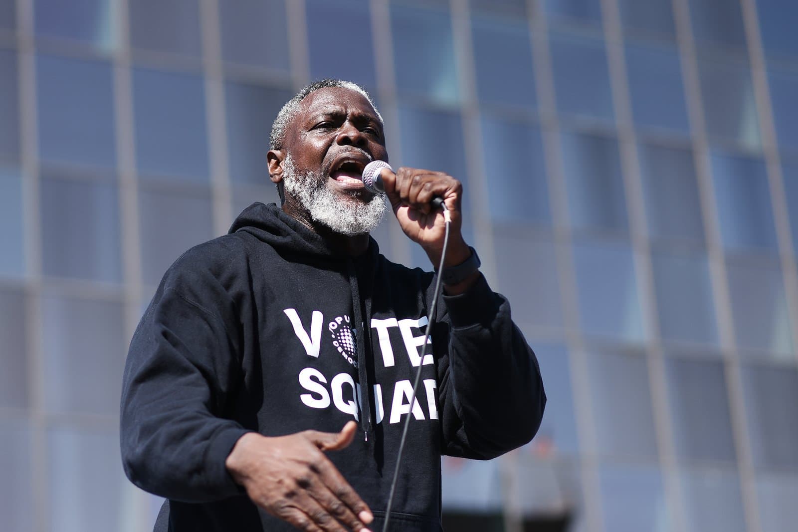 A man speaks into a microphone while wearing a Vote Squad hoodie during a No Kings protest in Anchorage, Alaska.