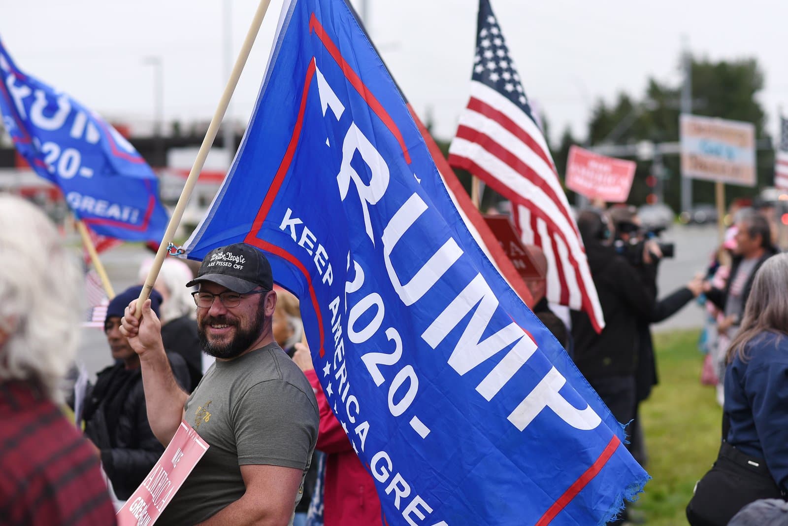 A man holds a Trump 2020 flag at a political rally in midtown Anchorage, Alaska, on a summer afternoon in August 2025.