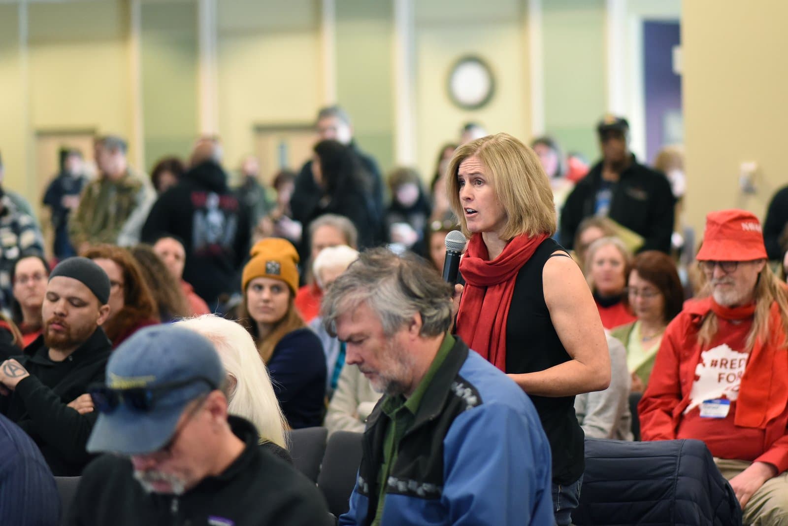 A woman speaks into a microphone during the 2024 Anchorage Legislative Town Hall, addressing an audience of community members in a public meeting.