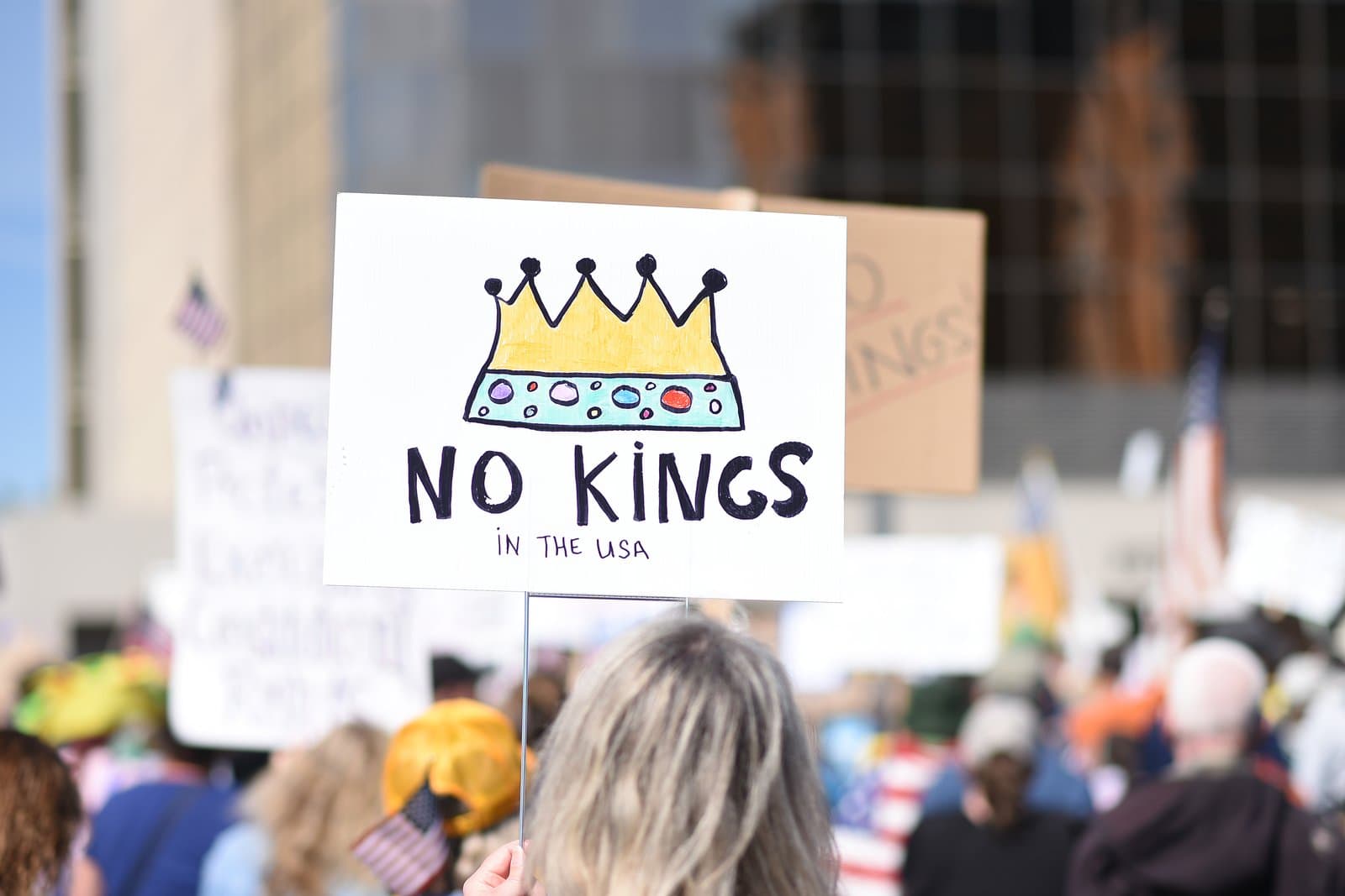 A protest sign reading No Kings in the USA with a colorful crown illustration held by a person at a public demonstration in Anchorage.