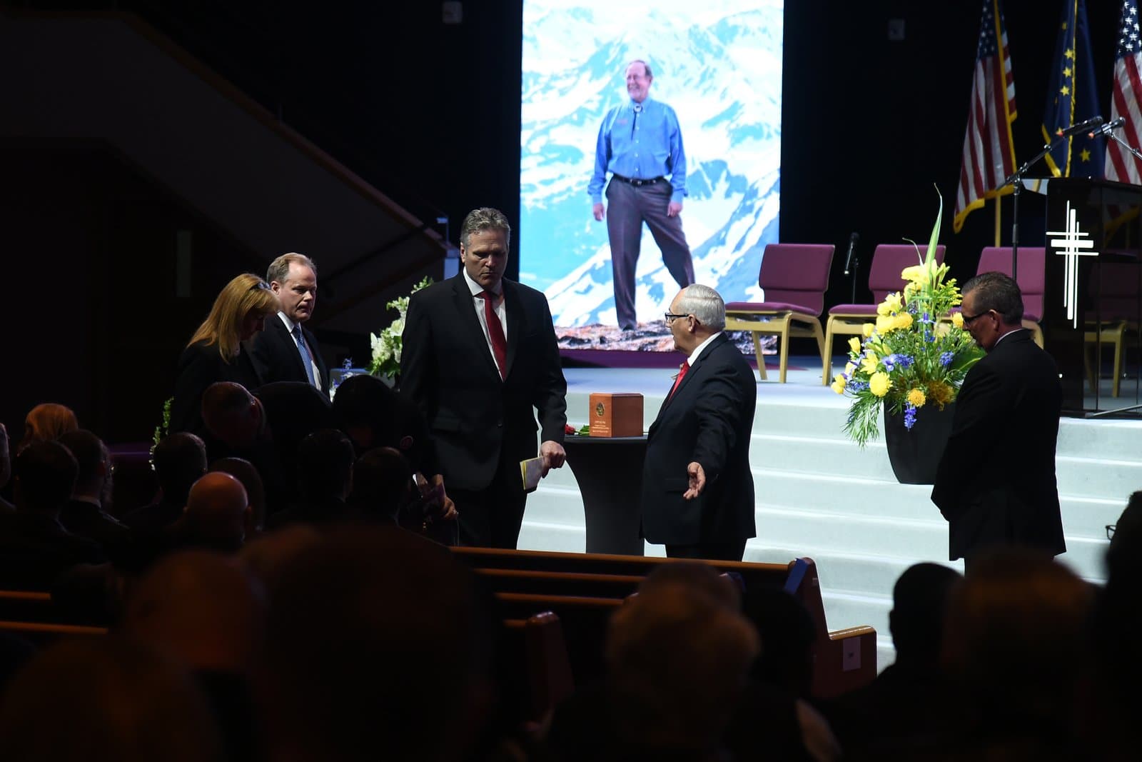 Attendees gather at a memorial service for Don Young, featuring a large portrait of the late congressman displayed on a stage.