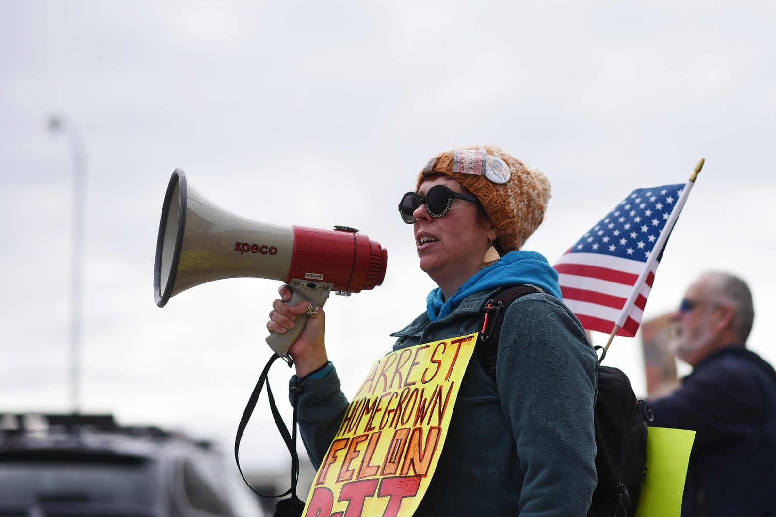 A protester wearing a knit hat and sunglasses speaks into a megaphone during an April 2025 demonstration in Anchorage, Alaska.