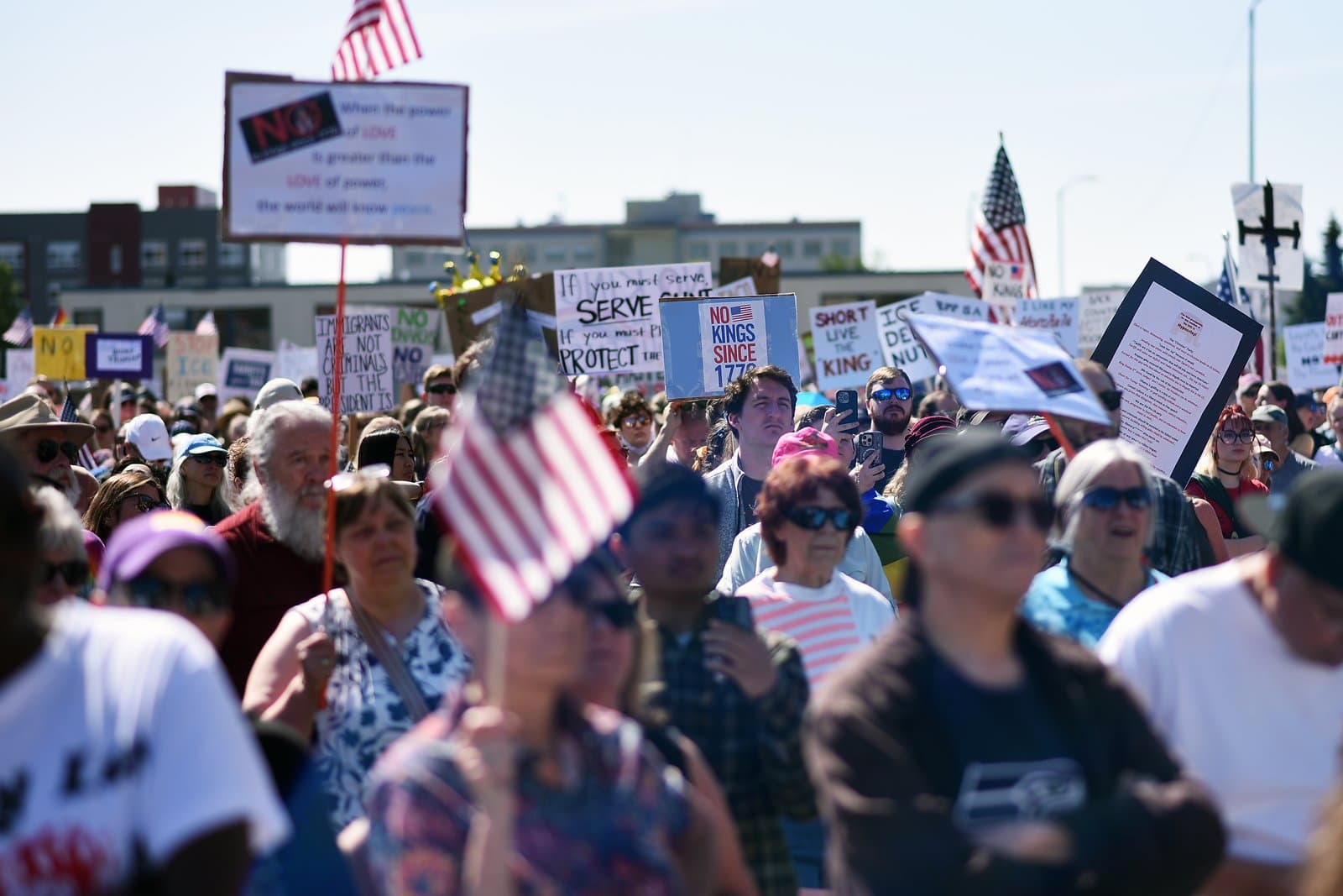Protesters carry signs and American flags during a public demonstration in Anchorage, Alaska, on a sunny June afternoon in 2025.