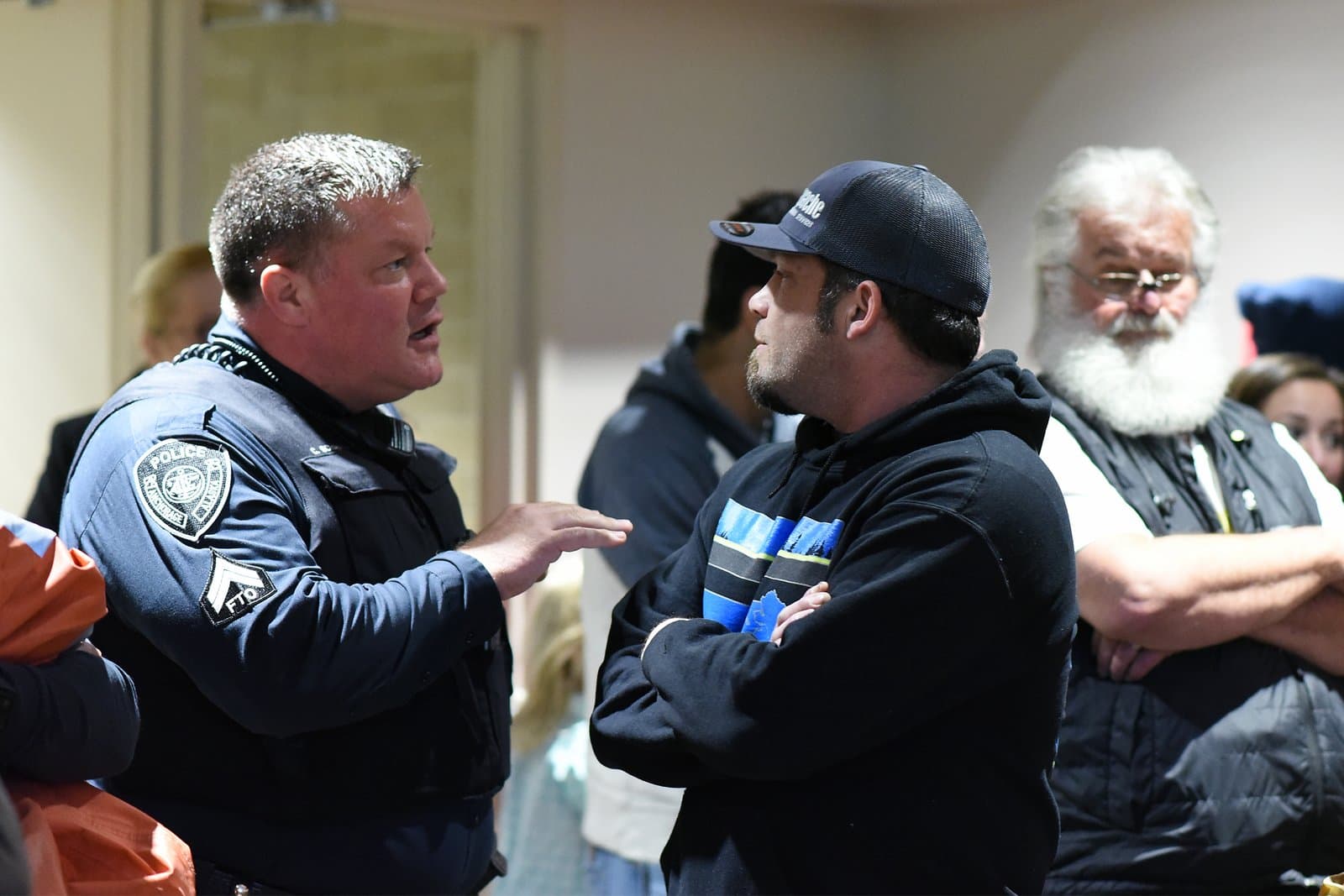 A police officer in uniform speaks to a man wearing a baseball cap during an Anchorage Assembly meeting in October 2021.