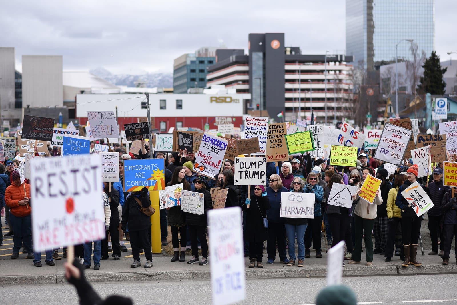 Protesters hold signs with political messages during a demonstration in Anchorage, Alaska, on a cloudy spring day in April 2025.