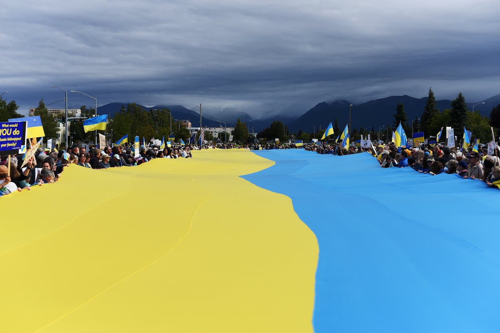 Protesters hold a massive Ukrainian flag during a demonstration in downtown Anchorage, Alaska, on a cloudy August afternoon in 2025.