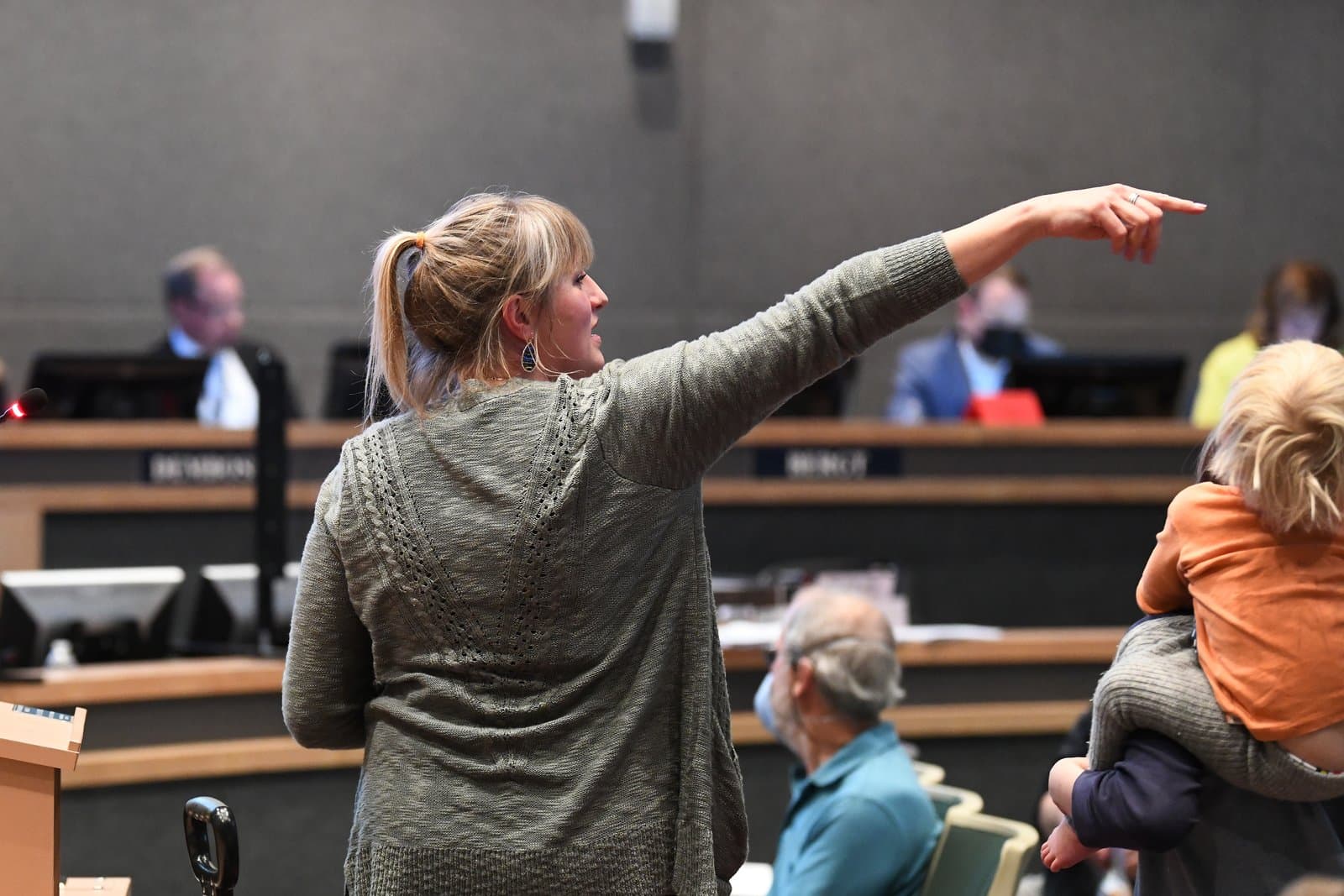A woman gestures while speaking at an Anchorage Assembly meeting in October 2021, holding a young child in her arms.