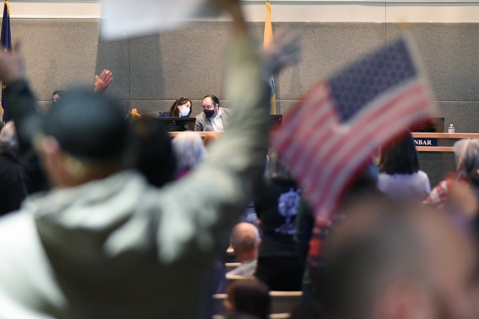 Citizens attend an Anchorage Assembly meeting in October 2021, featuring a person holding an American flag in the foreground.