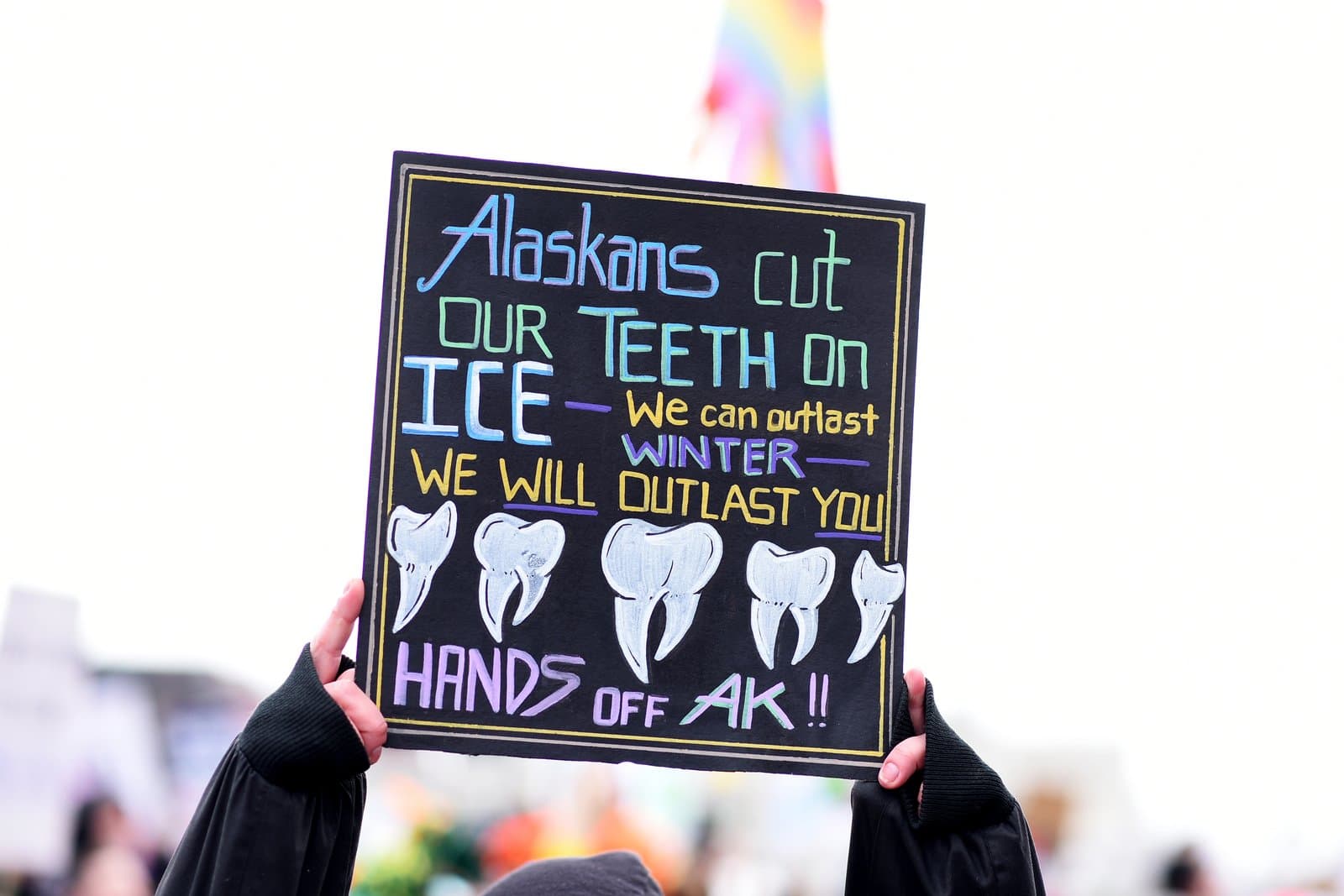 A protest sign held at an Anchorage rally features hand-drawn teeth and text declaring that Alaskans will outlast the winter and opposition.